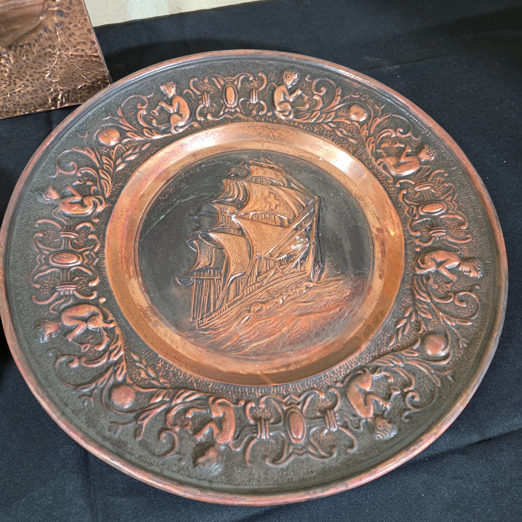 A collection of three vintage embossed metal decorative items, including a rectangular copper wall hanging and two round plates, all depicting sailing ships. - View 4
