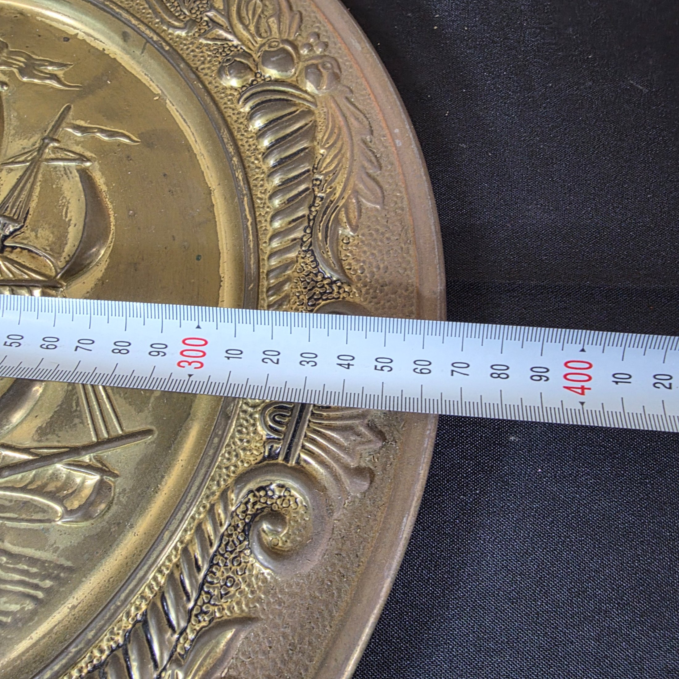 A collection of three vintage embossed metal decorative items, including a rectangular copper wall hanging and two round plates, all depicting sailing ships. - View 5