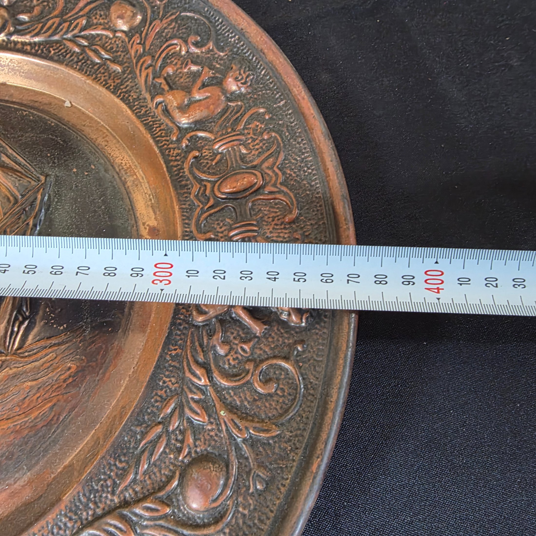 A collection of three vintage embossed metal decorative items, including a rectangular copper wall hanging and two round plates, all depicting sailing ships. - View 6