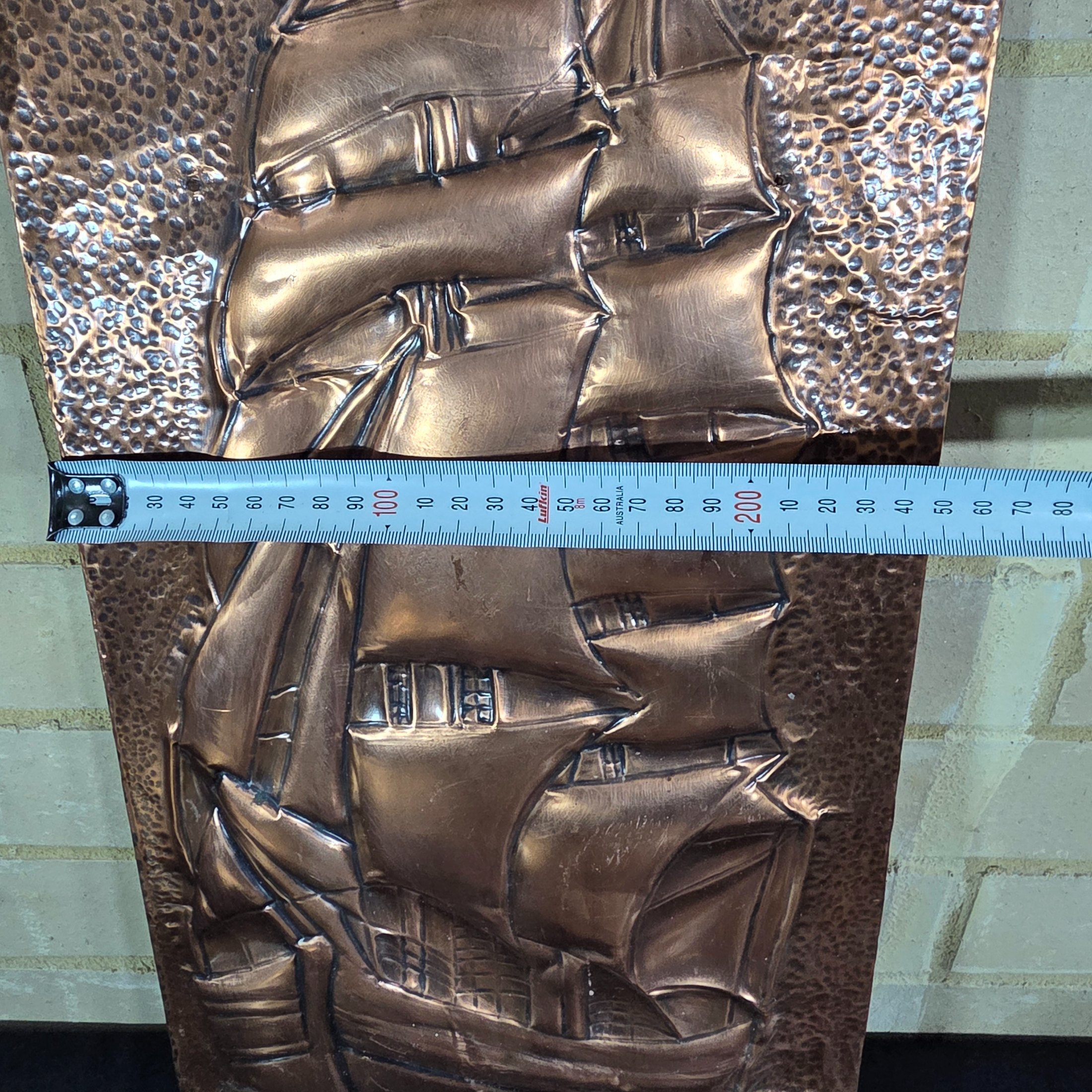 A collection of three vintage embossed metal decorative items, including a rectangular copper wall hanging and two round plates, all depicting sailing ships. - View 7