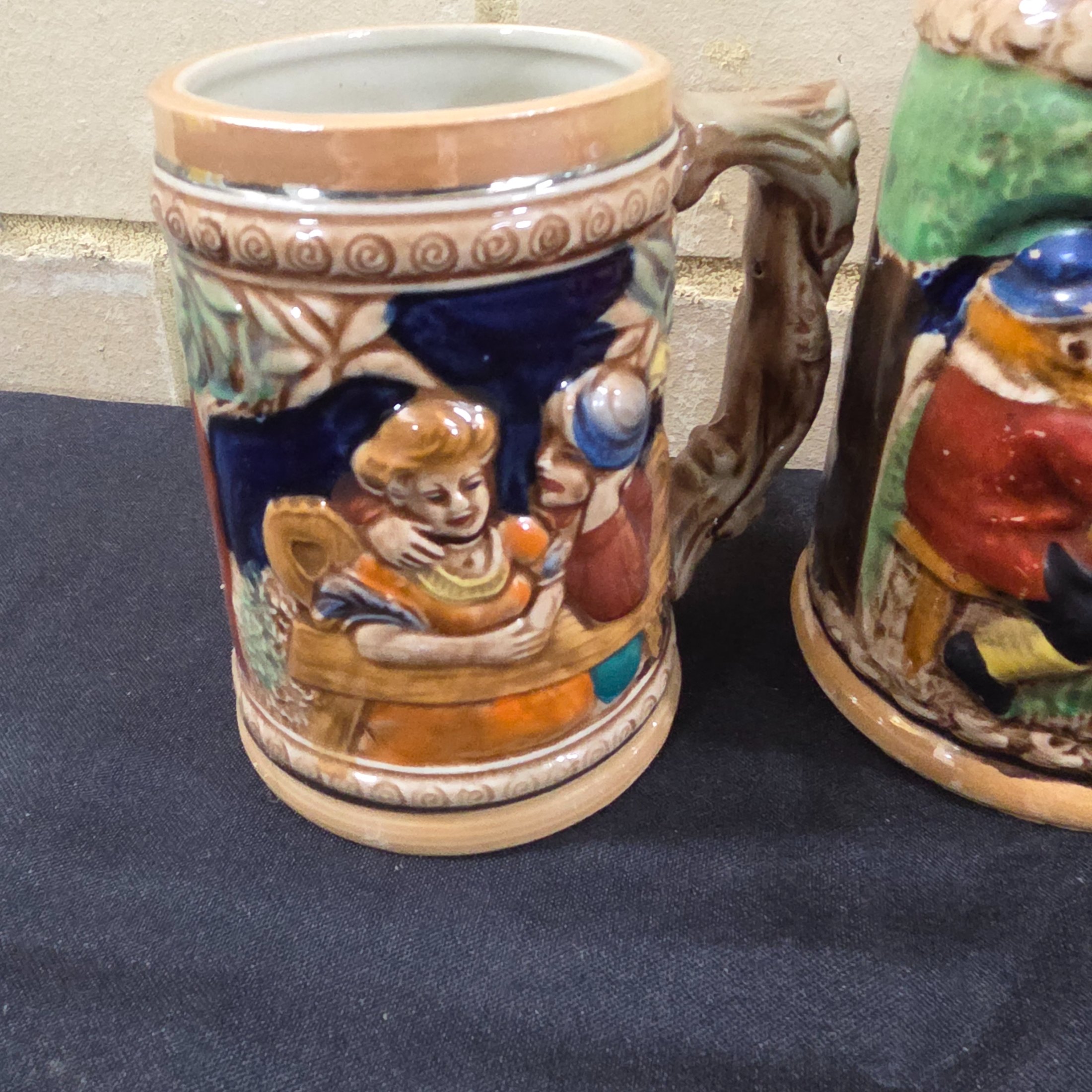 A set of four vintage Japanese ceramic mugs, designed in the style of traditional German beer steins, featuring intricate, hand-painted raised relief scenes depicting various Bavarian-themed activities and figures. - View 2
