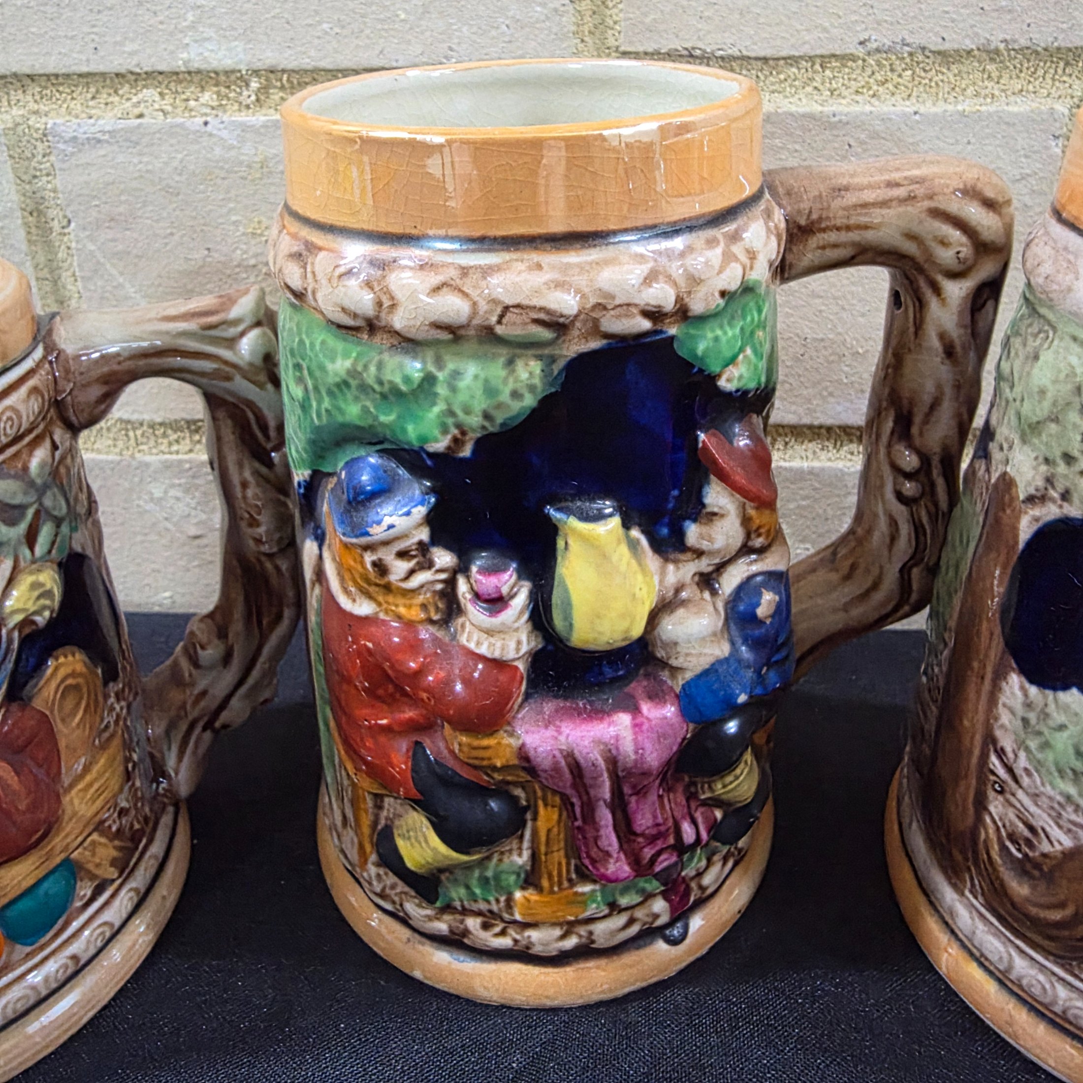A set of four vintage Japanese ceramic mugs, designed in the style of traditional German beer steins, featuring intricate, hand-painted raised relief scenes depicting various Bavarian-themed activities and figures. - View 3