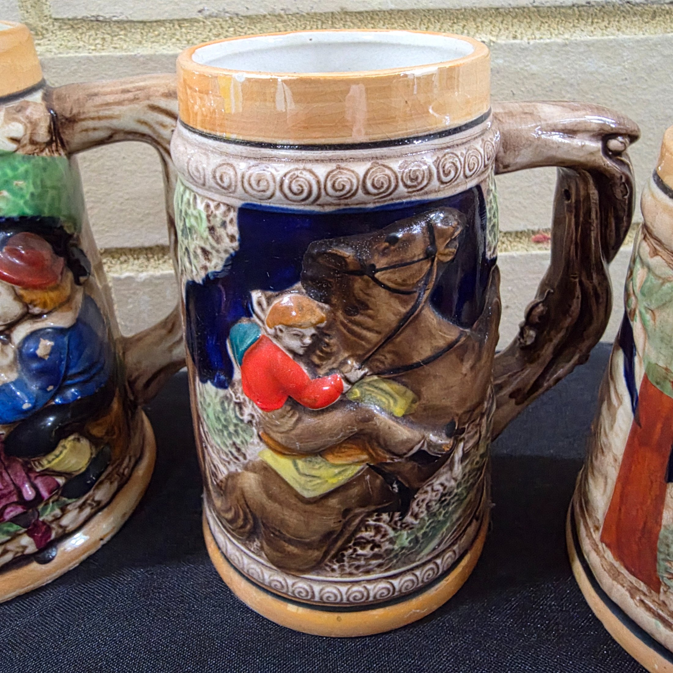 A set of four vintage Japanese ceramic mugs, designed in the style of traditional German beer steins, featuring intricate, hand-painted raised relief scenes depicting various Bavarian-themed activities and figures. - View 4