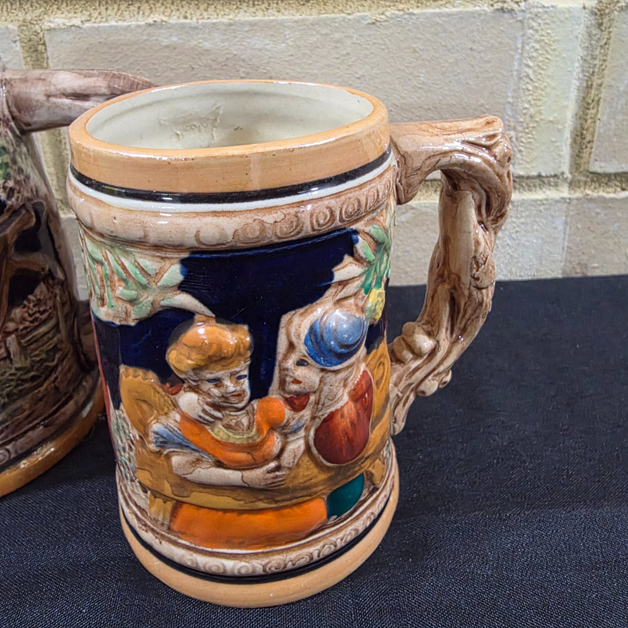 A set of four vintage Japanese ceramic mugs, designed in the style of traditional German beer steins, featuring intricate, hand-painted raised relief scenes depicting various Bavarian-themed activities and figures. - View 5