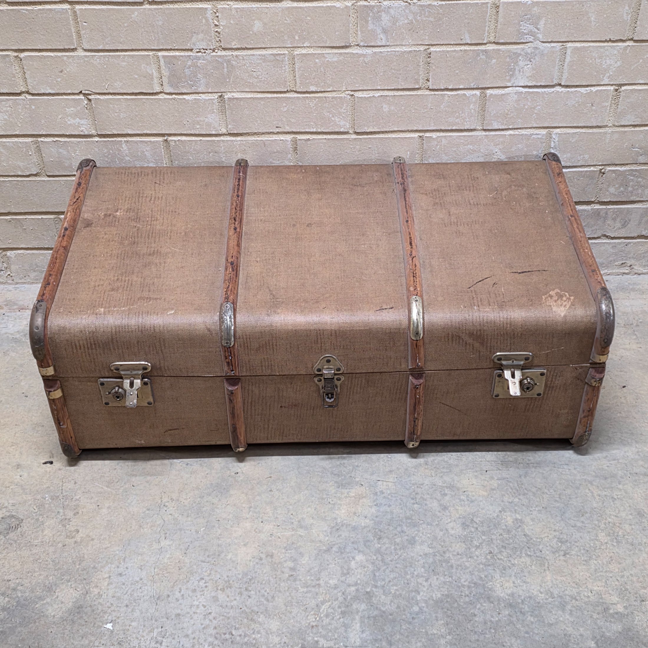 A classic vintage travel trunk from the early 20th century, made from woven fabric over a wooden frame with reinforcing wooden slats and metal hardware.