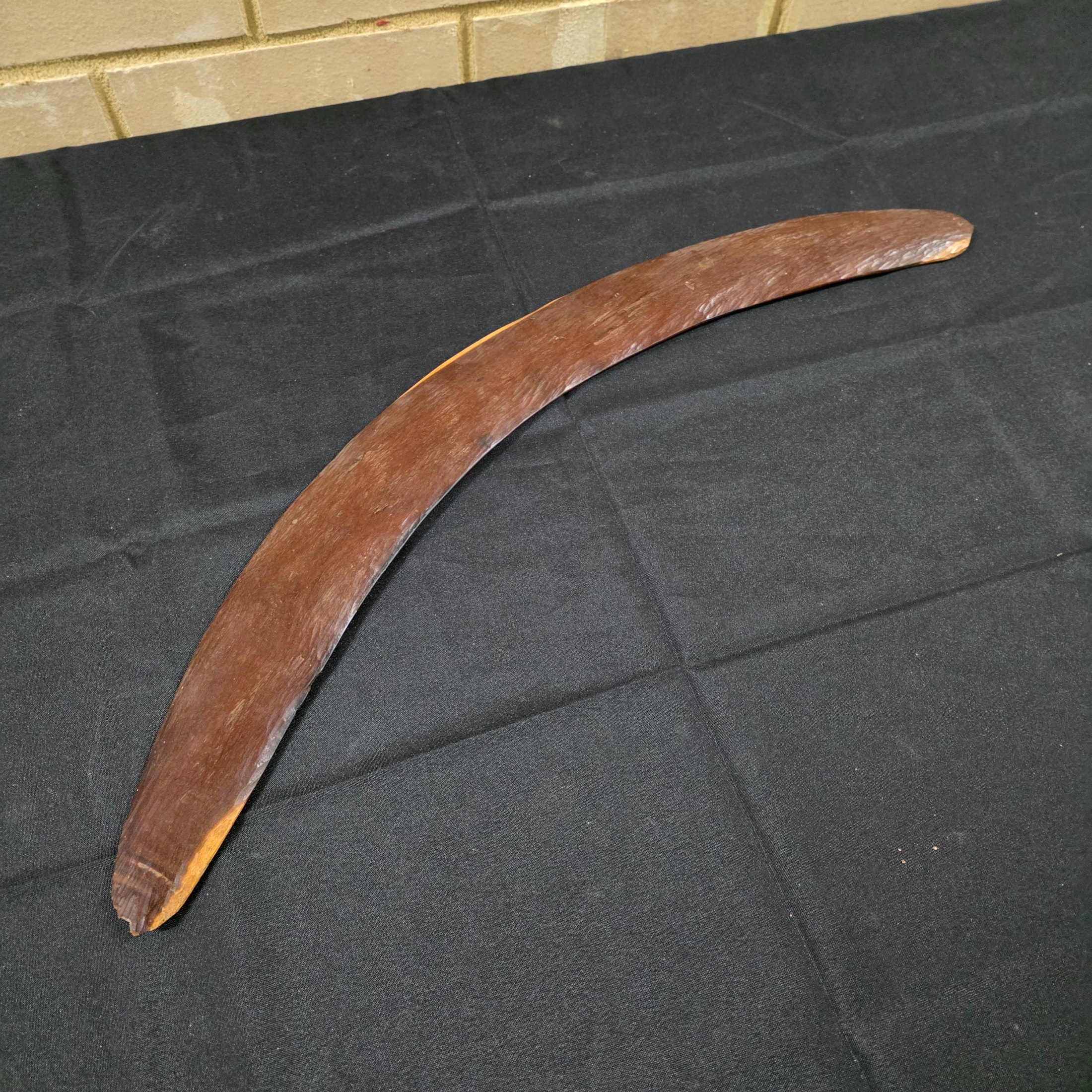 A vintage hand-carved wooden boomerang with a natural dark brown finish, approximately 62cm in length.