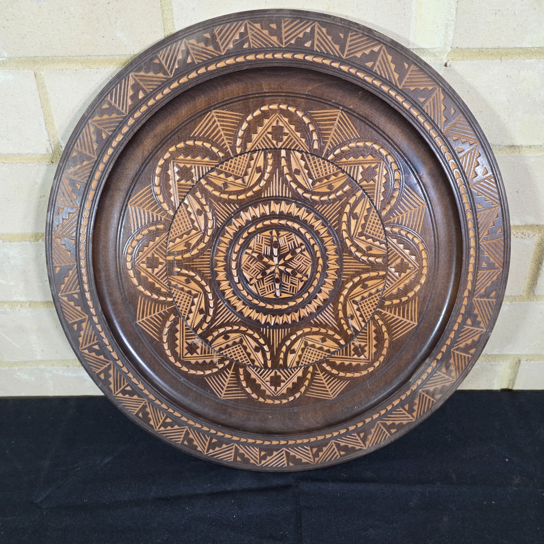 A vintage hand-carved wooden decorative plate, featuring intricate geometric and radial chip-carved patterns revealing lighter wood beneath a dark stain, likely mid-20th century.