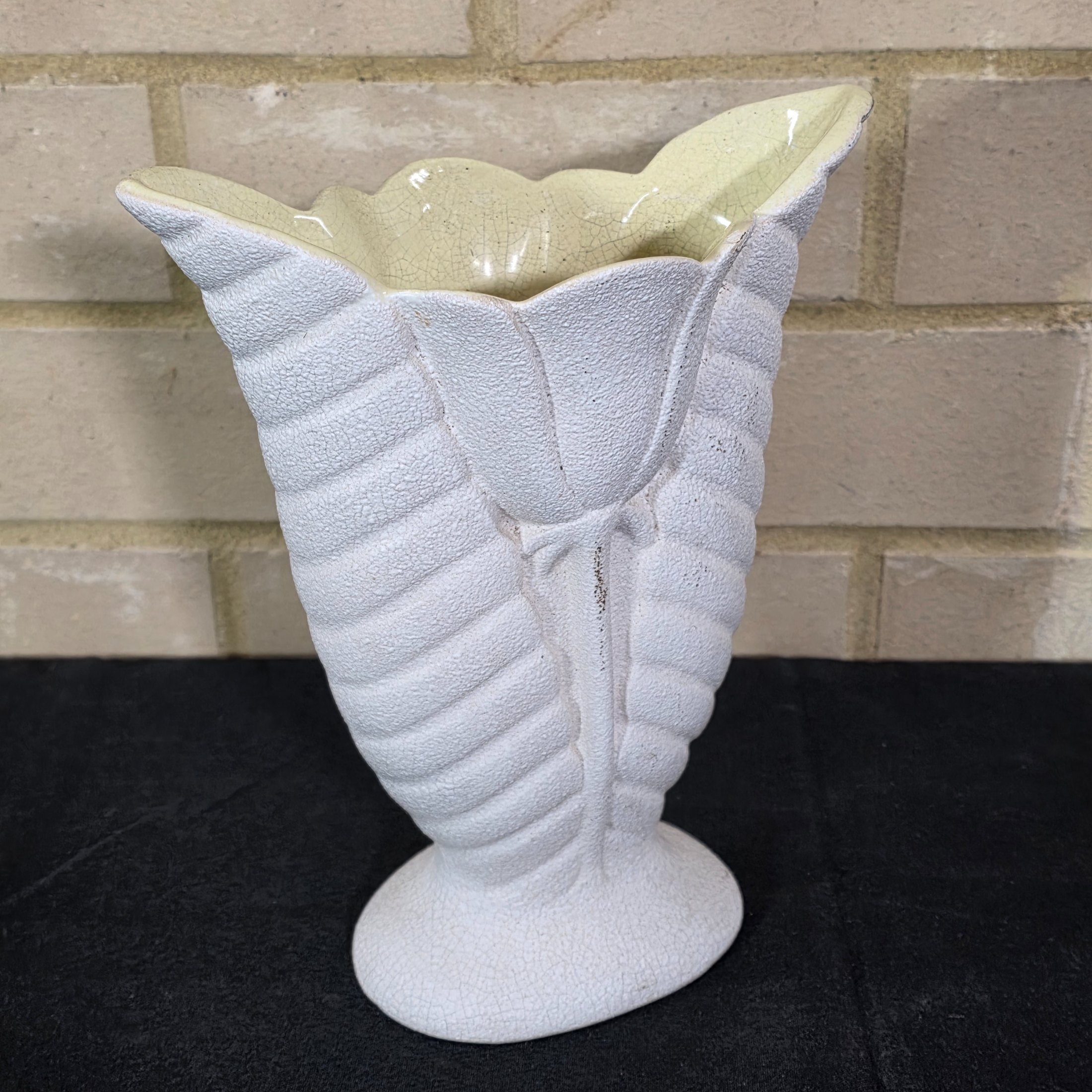 A striking white ceramic vase, likely from the mid-20th century, distinguished by its textured, fluted body reminiscent of a shell or stylized leaf. The piece features a prominent crackle glaze on both its off-white exterior and pale yellow interior.