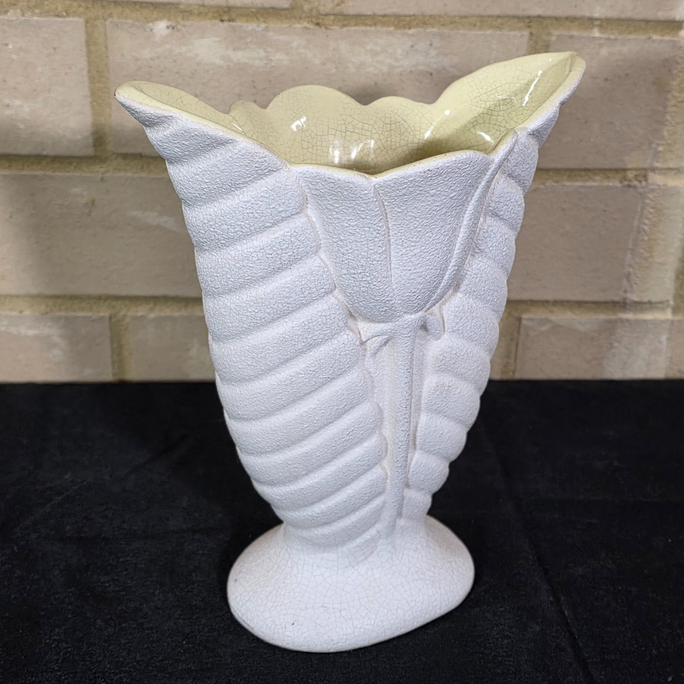 A striking white ceramic vase, likely from the mid-20th century, distinguished by its textured, fluted body reminiscent of a shell or stylized leaf. The piece features a prominent crackle glaze on both its off-white exterior and pale yellow interior. - View 3