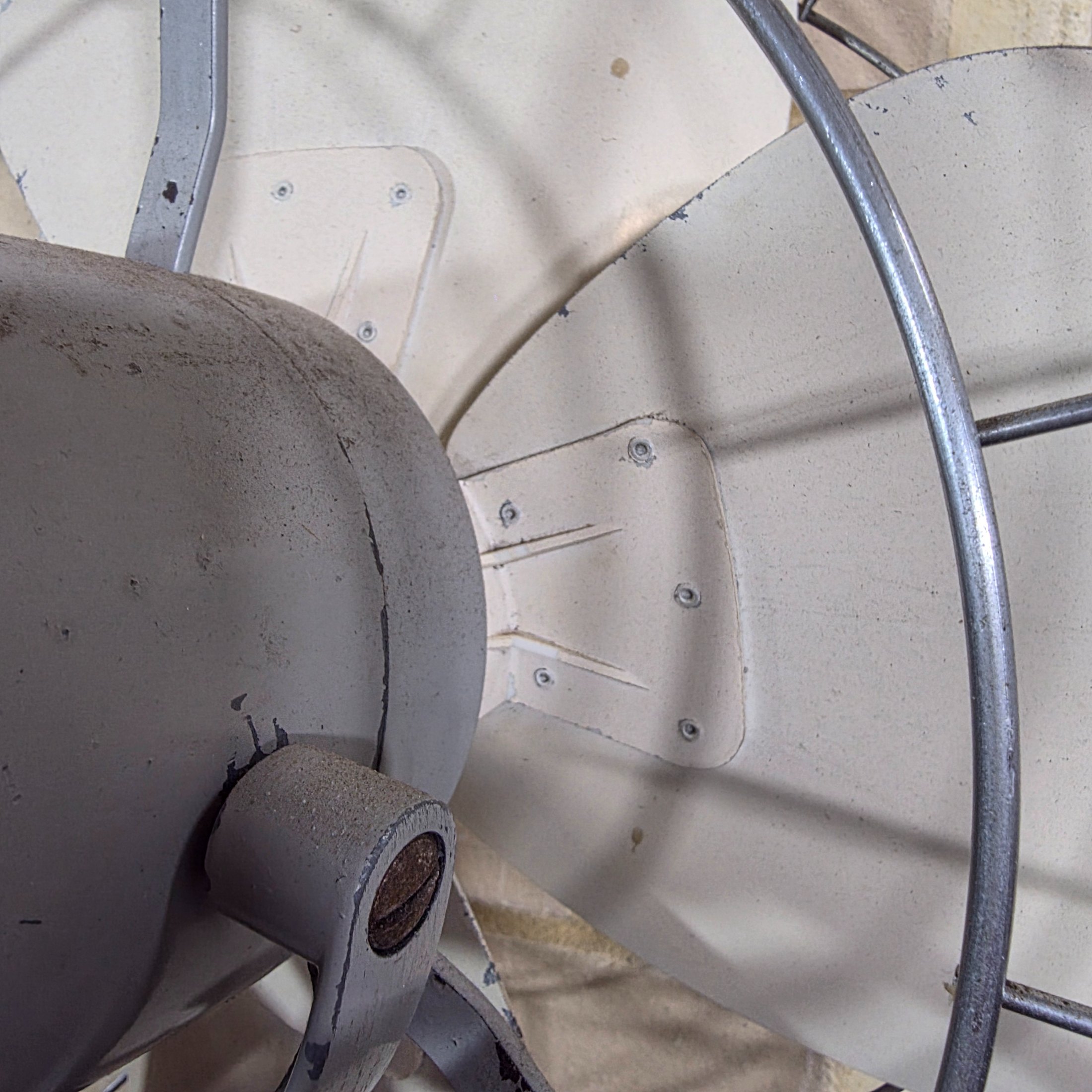 A vintage Mistral electric fan, likely from the mid-20th century, featuring a grey painted metal base and motor housing, a chrome wire cage, and cream plastic blades, with a visible red Mistral logo on the front grille. - View 4