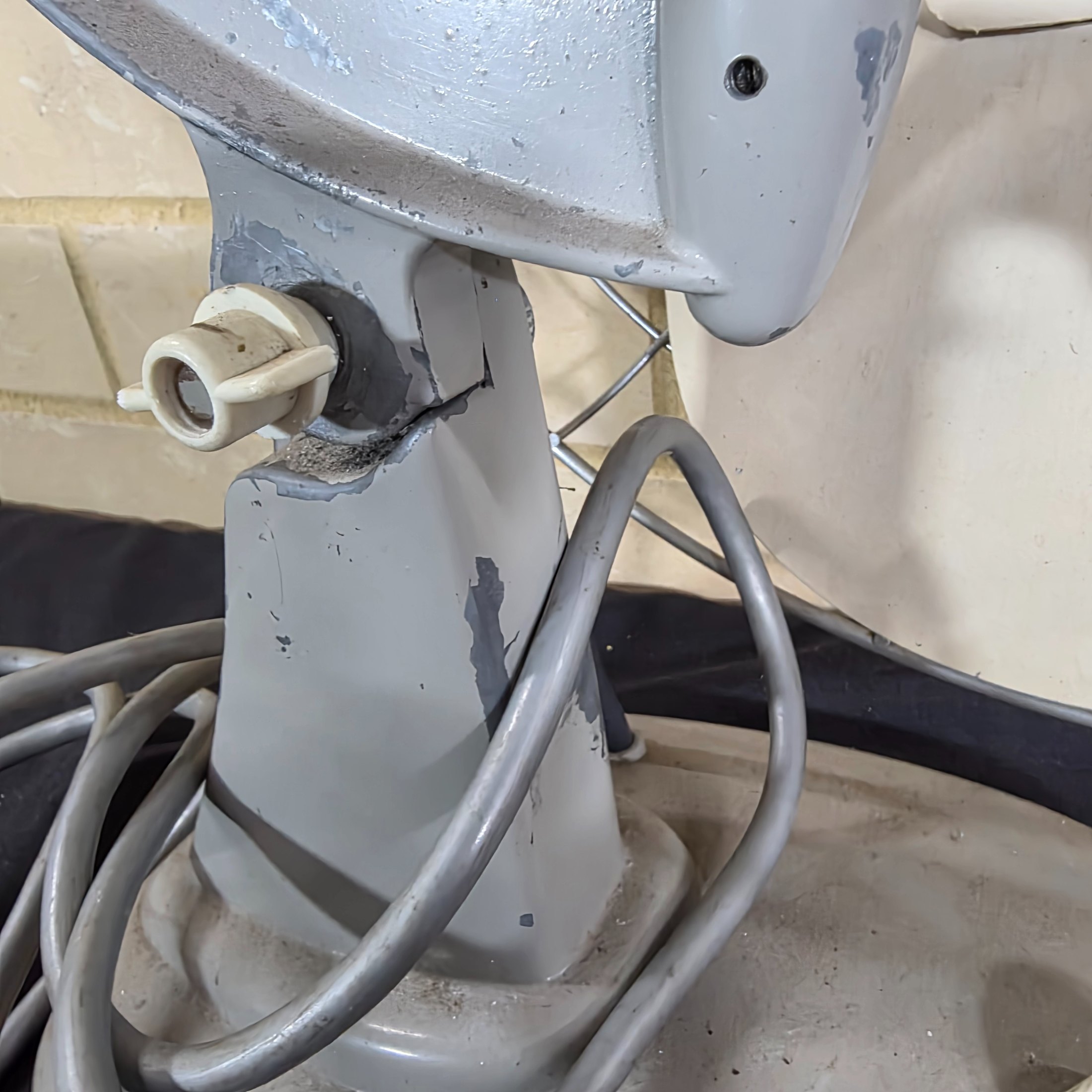 A vintage Mistral electric fan, likely from the mid-20th century, featuring a grey painted metal base and motor housing, a chrome wire cage, and cream plastic blades, with a visible red Mistral logo on the front grille. - View 7