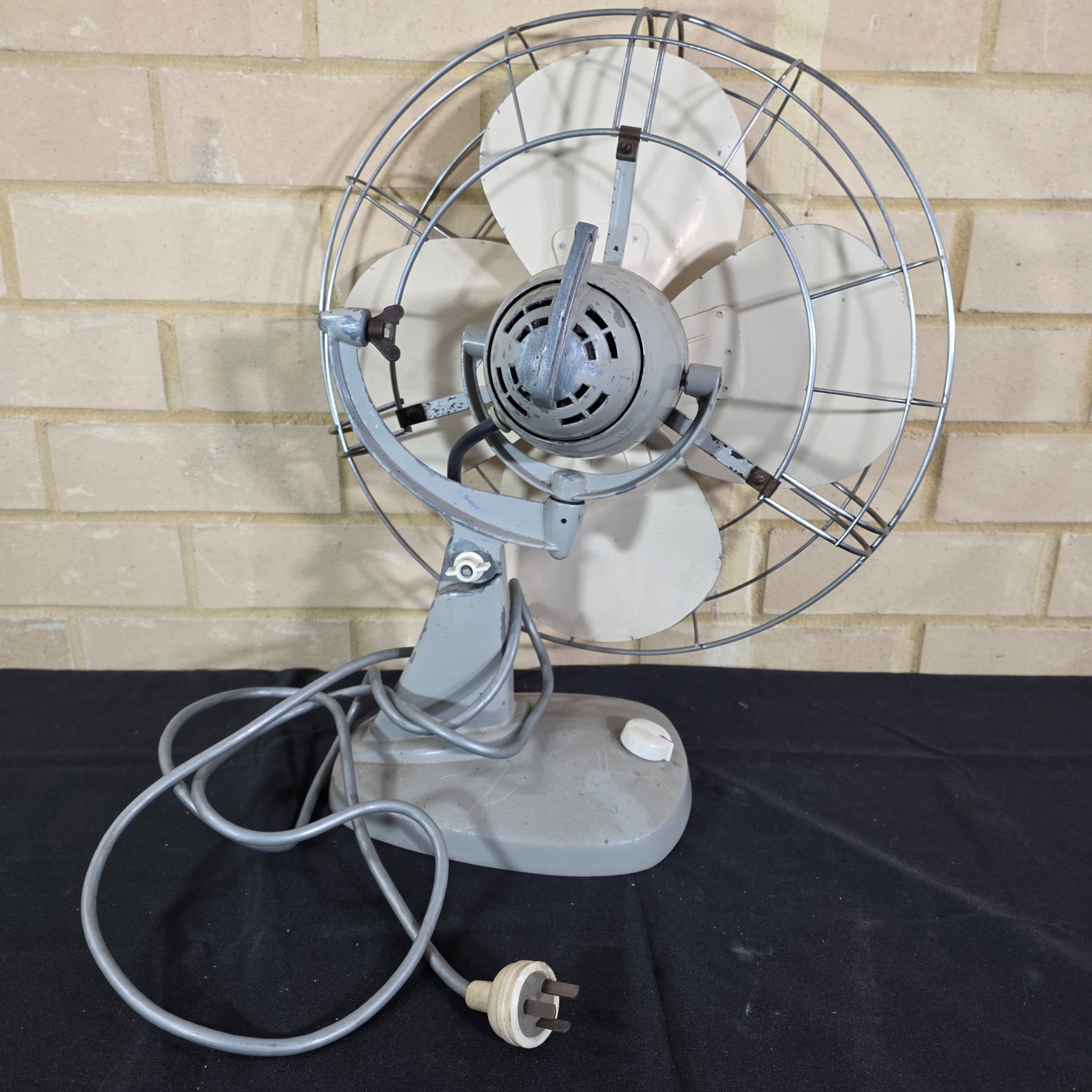 A vintage Mistral electric fan, likely from the mid-20th century, featuring a grey painted metal base and motor housing, a chrome wire cage, and cream plastic blades, with a visible red Mistral logo on the front grille. - View 8