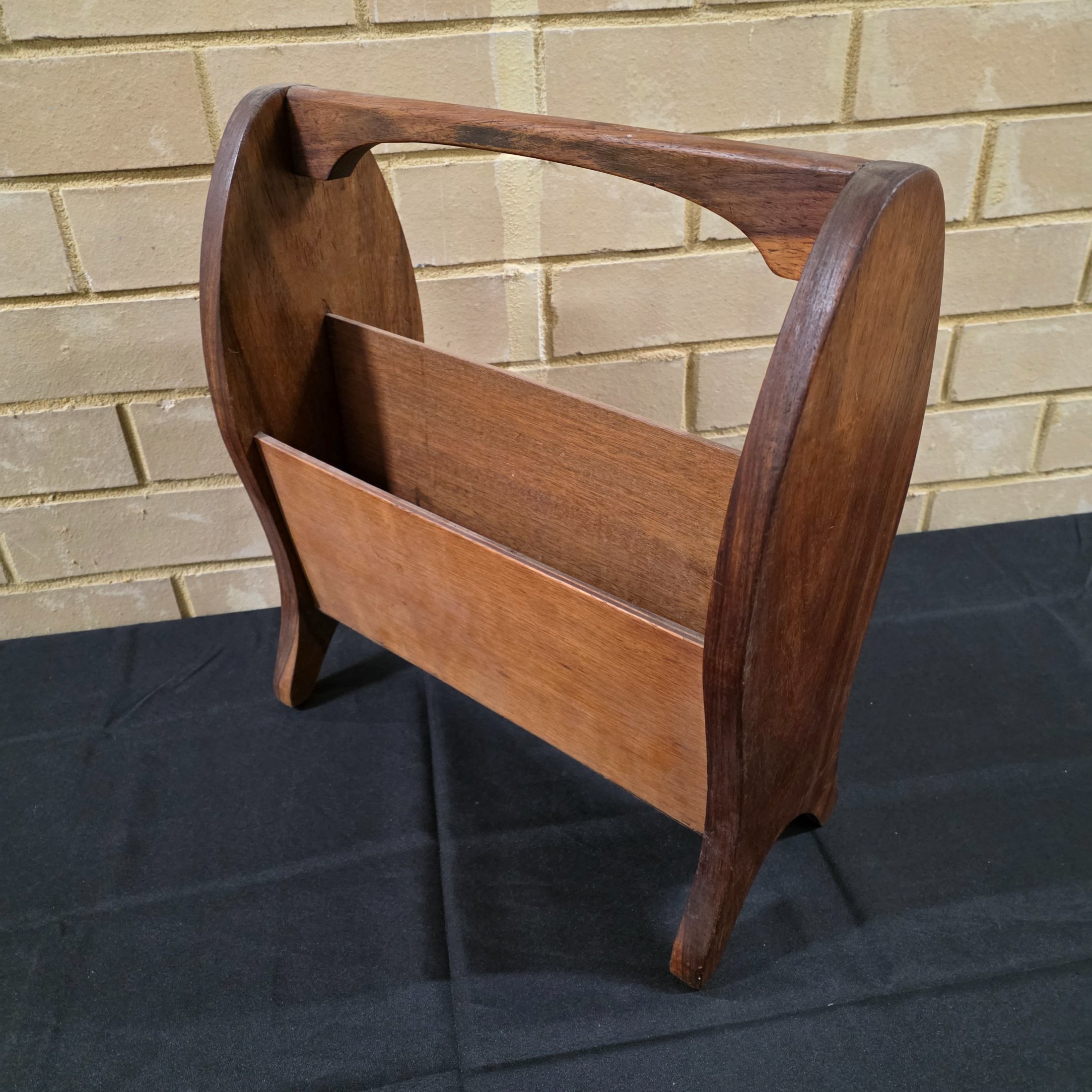 A classic vintage mid-century wooden magazine rack, featuring a curved handle and two functional compartments for storage. This piece showcases the simple, elegant design characteristic of its era, crafted from solid wood with a warm, natural finish.