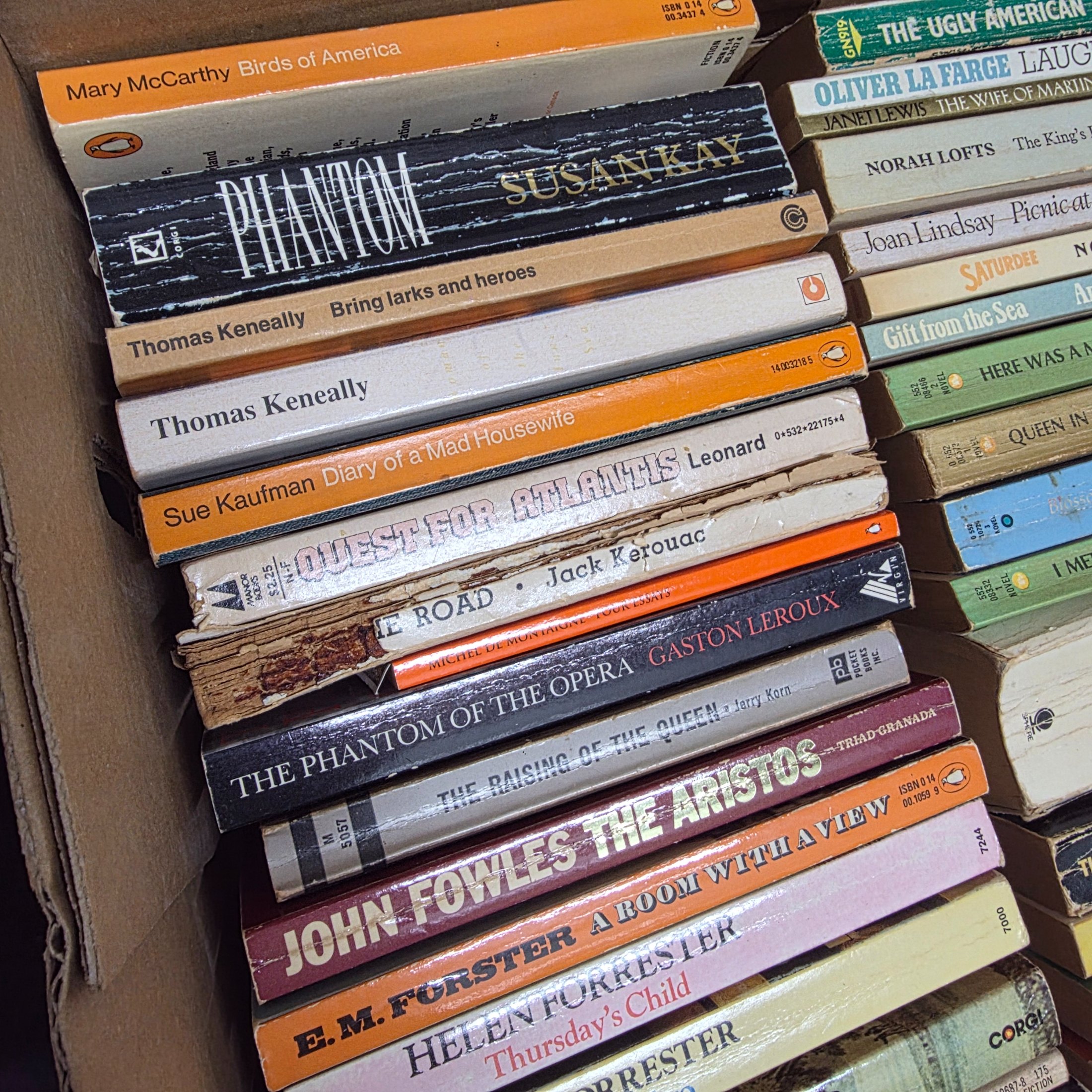 A large collection of assorted paperback and hardcover books, stacked in multiple cardboard boxes. - View 6