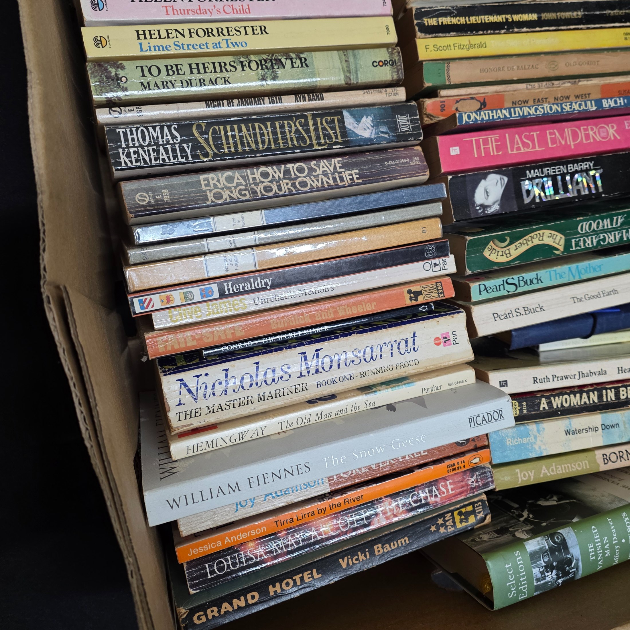 A large collection of assorted paperback and hardcover books, stacked in multiple cardboard boxes. - View 8