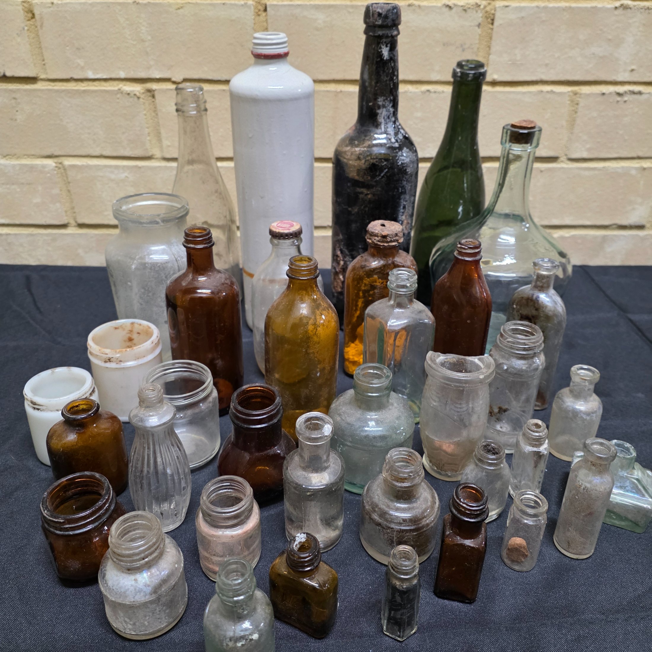 A diverse collection of antique and vintage glass and ceramic bottles and jars, dating from the late 19th to mid-20th century, showcasing various styles and materials.