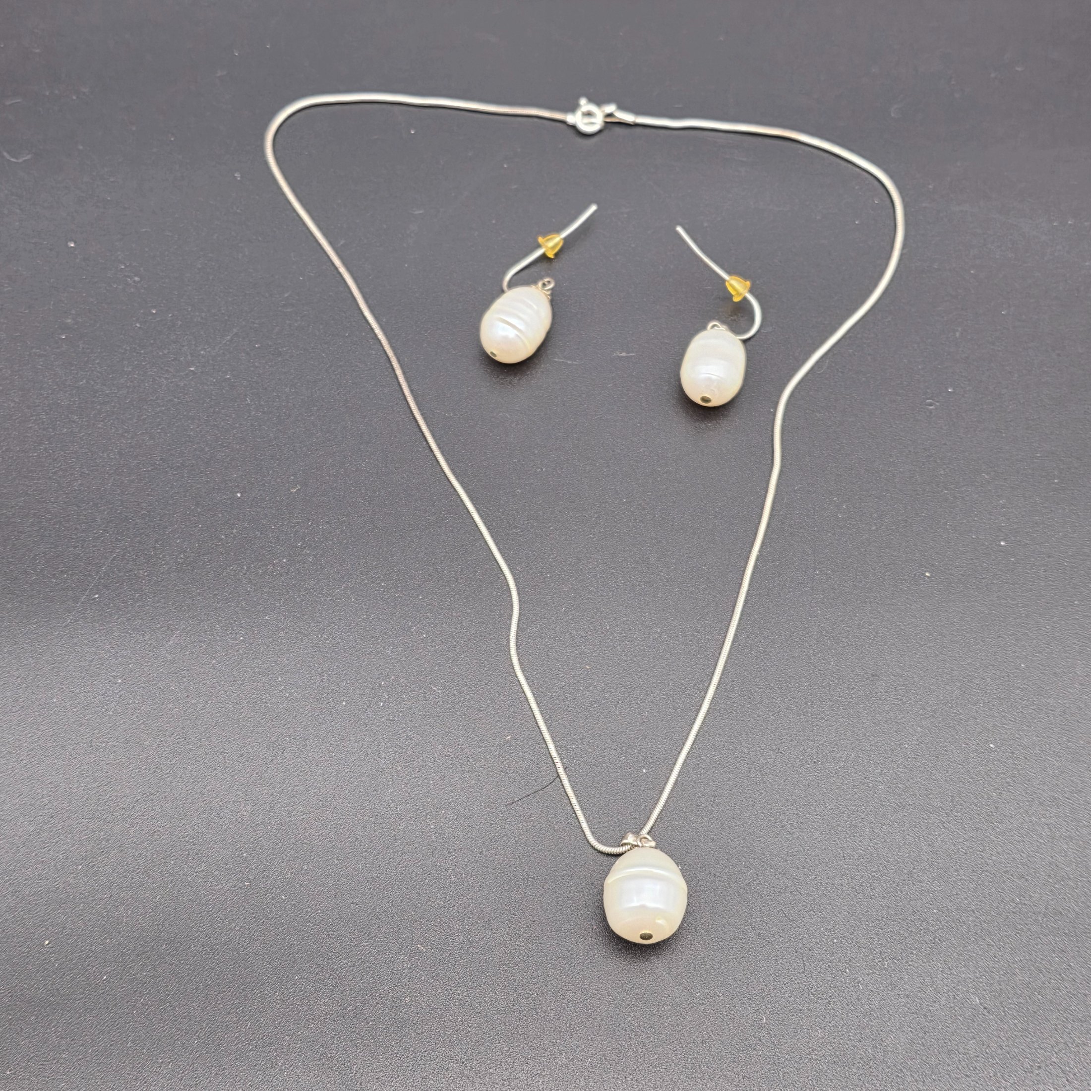 A matching Paul Kennedy sterling silver and baroque freshwater pearl necklace and earring set. This contemporary jewellery suite features a snake chain necklace with a single irregular pearl pendant and a pair of coordinating hook earrings, each set with a baroque pearl.