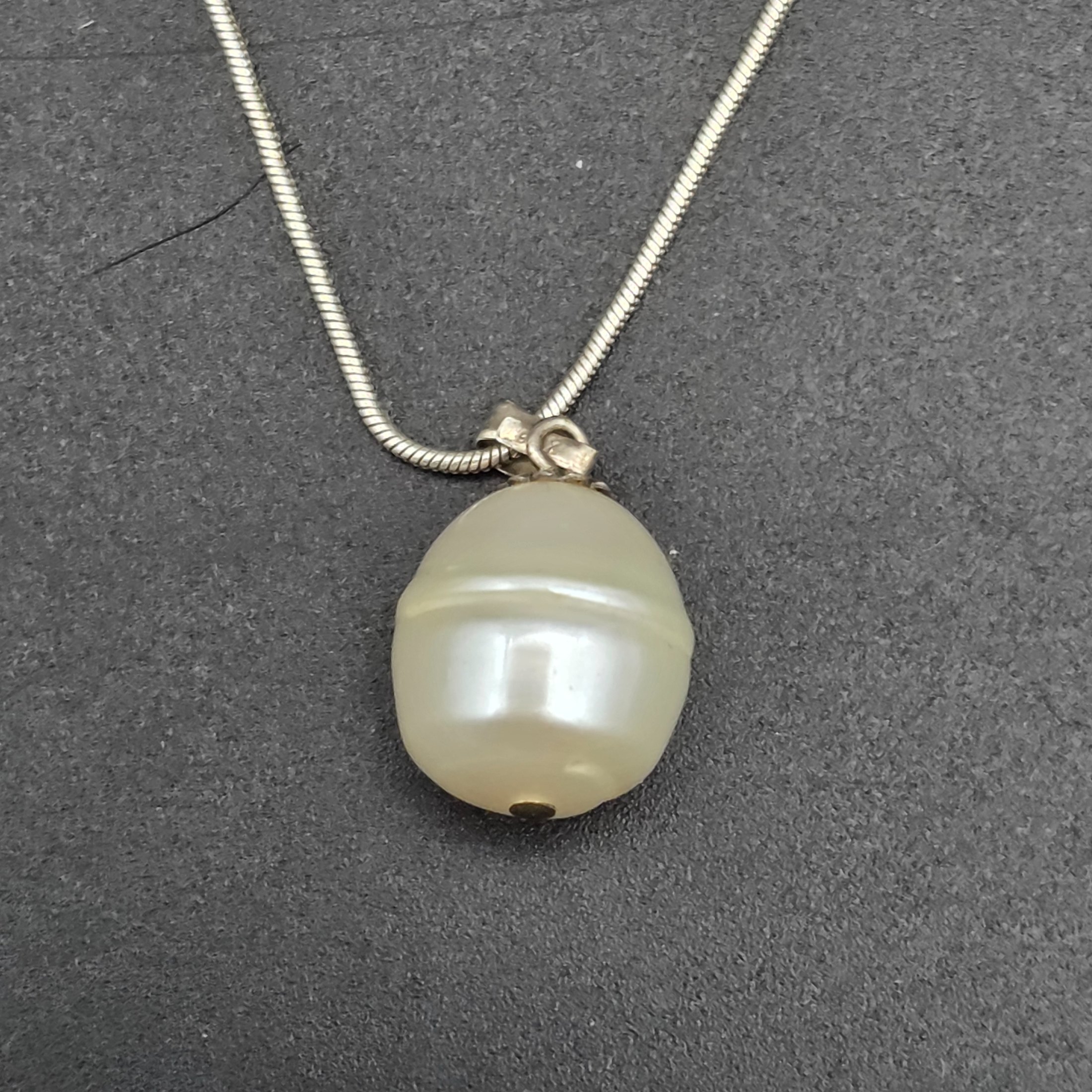 A matching Paul Kennedy sterling silver and baroque freshwater pearl necklace and earring set. This contemporary jewellery suite features a snake chain necklace with a single irregular pearl pendant and a pair of coordinating hook earrings, each set with a baroque pearl. - View 2