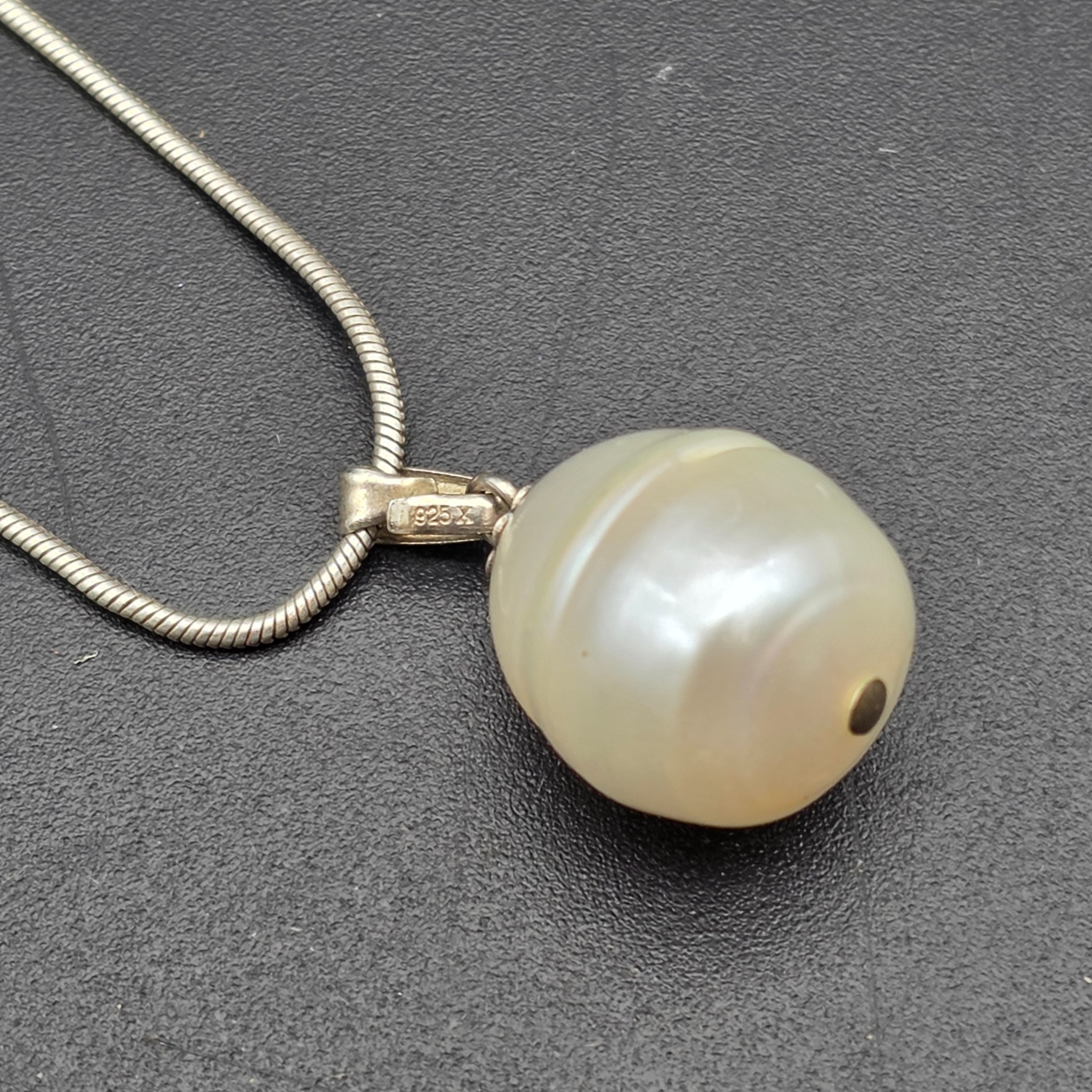A matching Paul Kennedy sterling silver and baroque freshwater pearl necklace and earring set. This contemporary jewellery suite features a snake chain necklace with a single irregular pearl pendant and a pair of coordinating hook earrings, each set with a baroque pearl. - View 3