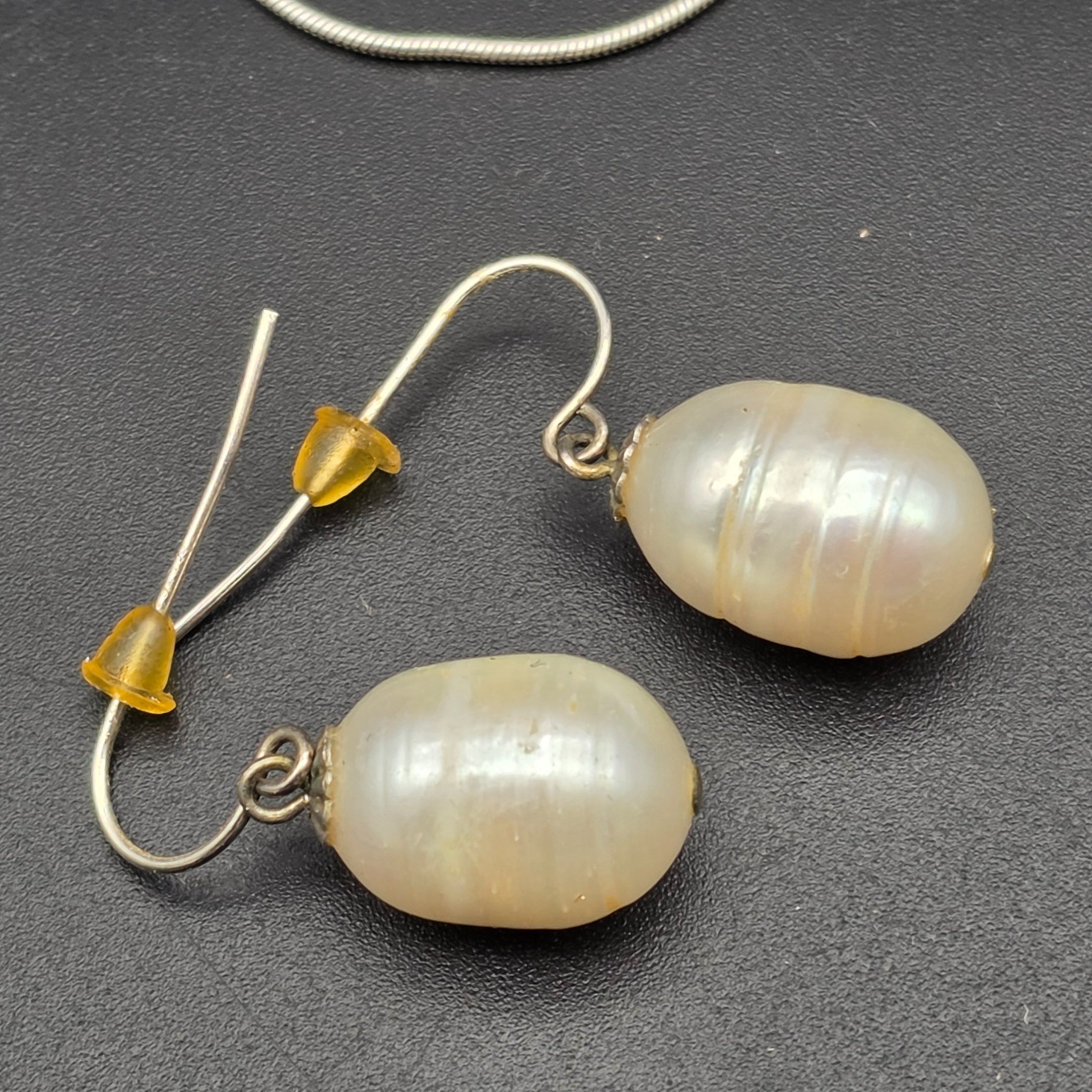 A matching Paul Kennedy sterling silver and baroque freshwater pearl necklace and earring set. This contemporary jewellery suite features a snake chain necklace with a single irregular pearl pendant and a pair of coordinating hook earrings, each set with a baroque pearl. - View 5