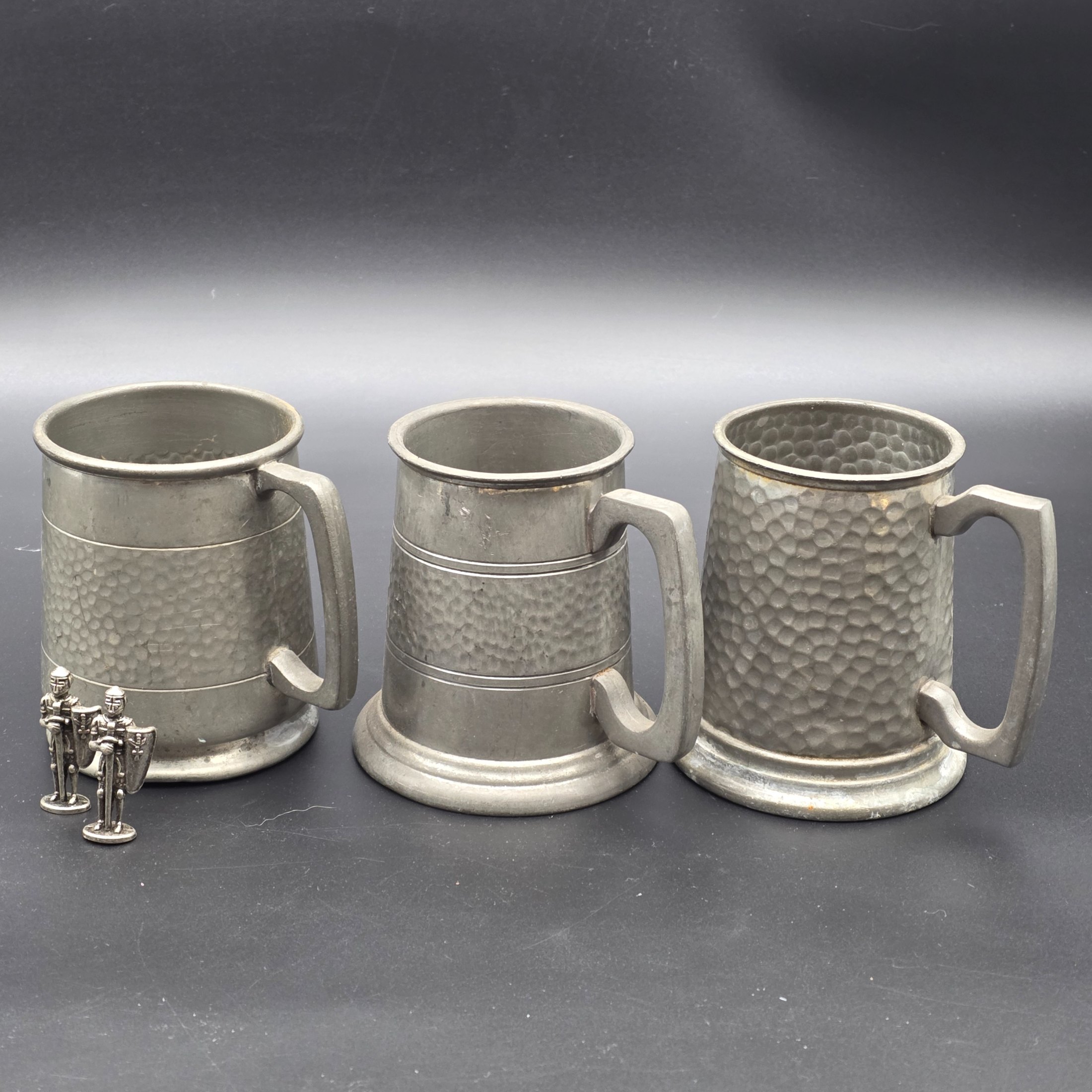 A collection featuring three vintage pewter tankards and two small pewter knight figurines, showcasing different manufacturing origins and finishes from the mid to late 20th century.