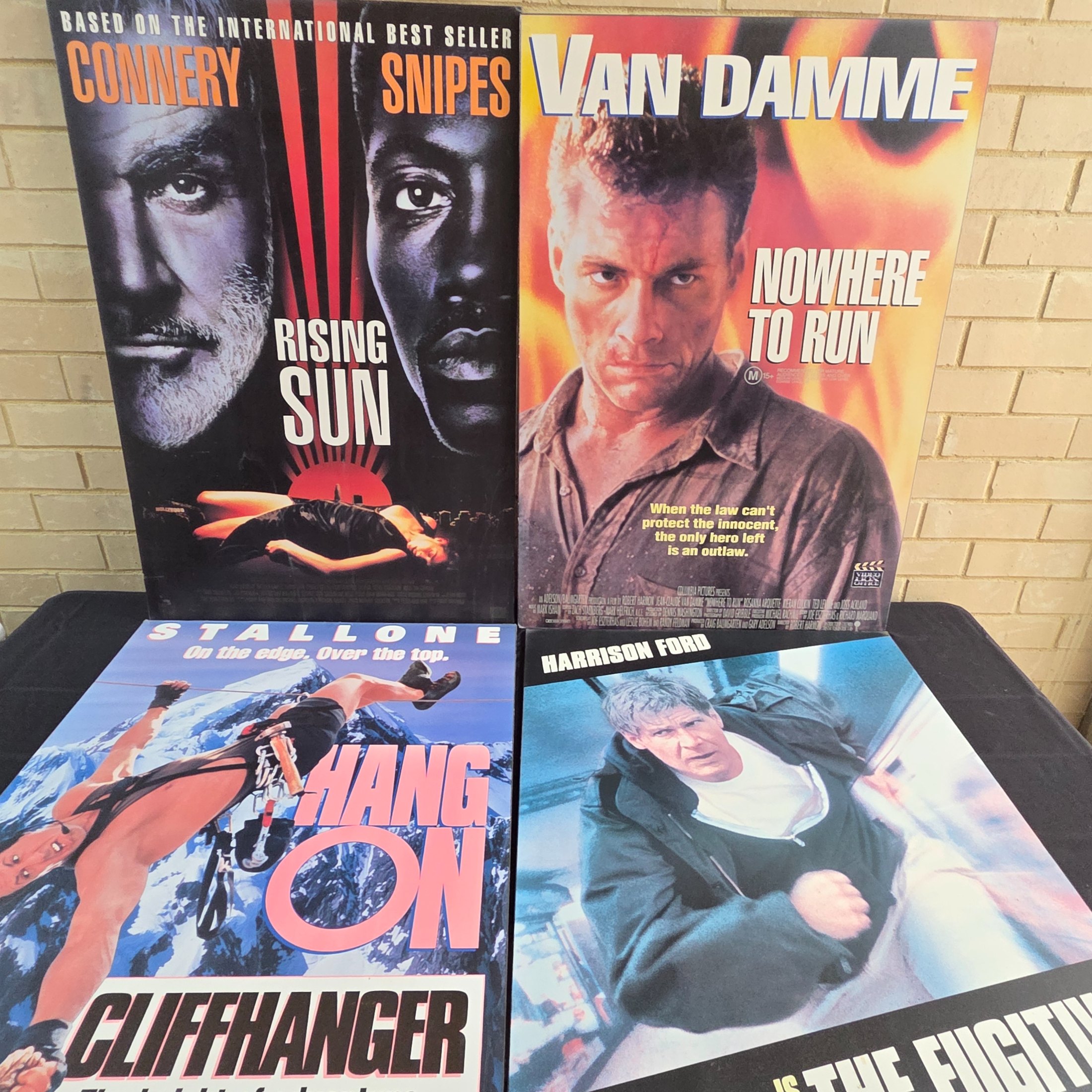 Four mounted original movie posters from the early 1990s, featuring classic action films 'Rising Sun', 'Nowhere to Run', 'Cliffhanger', and 'The Fugitive'.