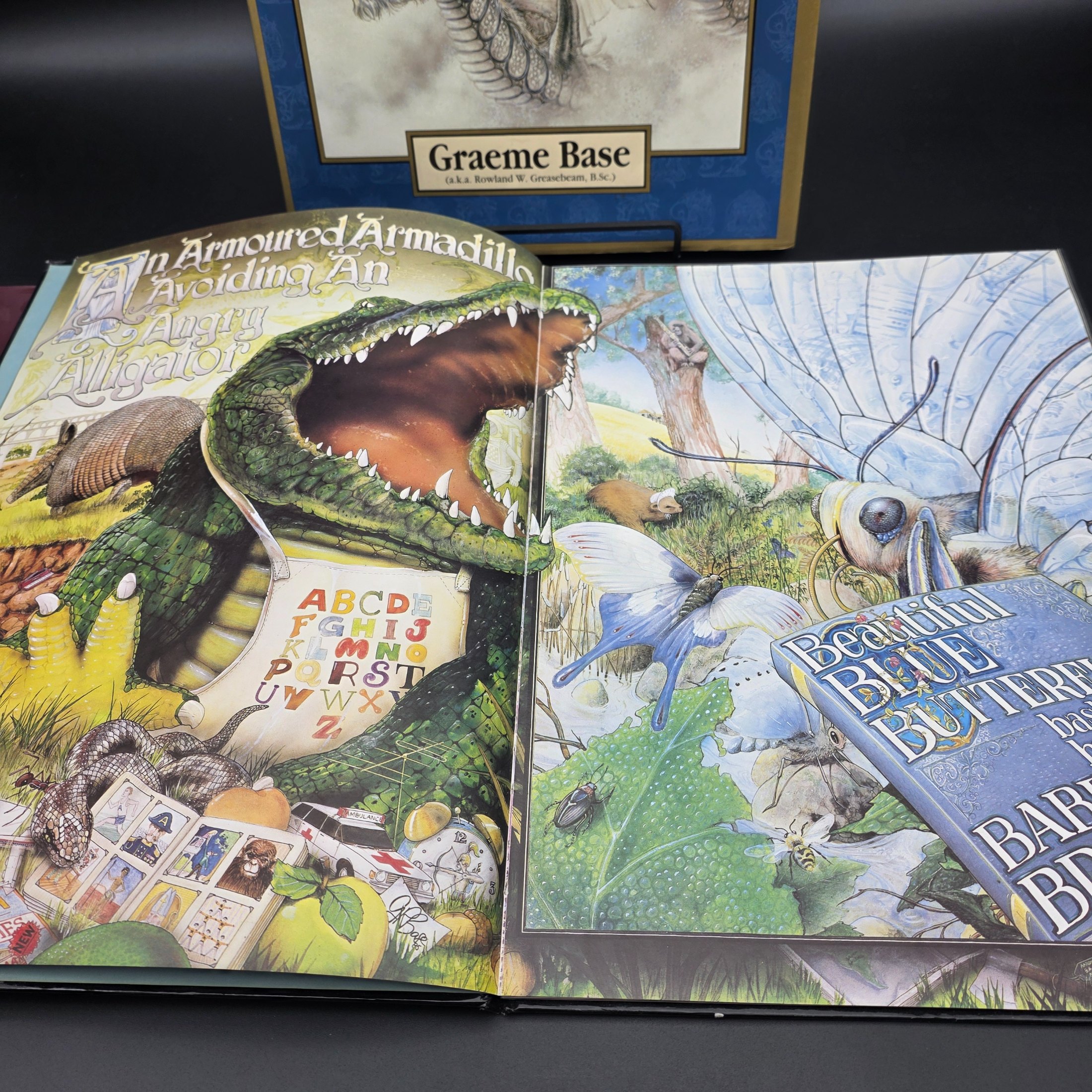 A collection of three hardcover children's books by Graeme Base: 'The Discovery of Dragons', 'The Eleventh Hour Curious Mystery', and 'Animalia', featuring intricate illustrations. - View 8