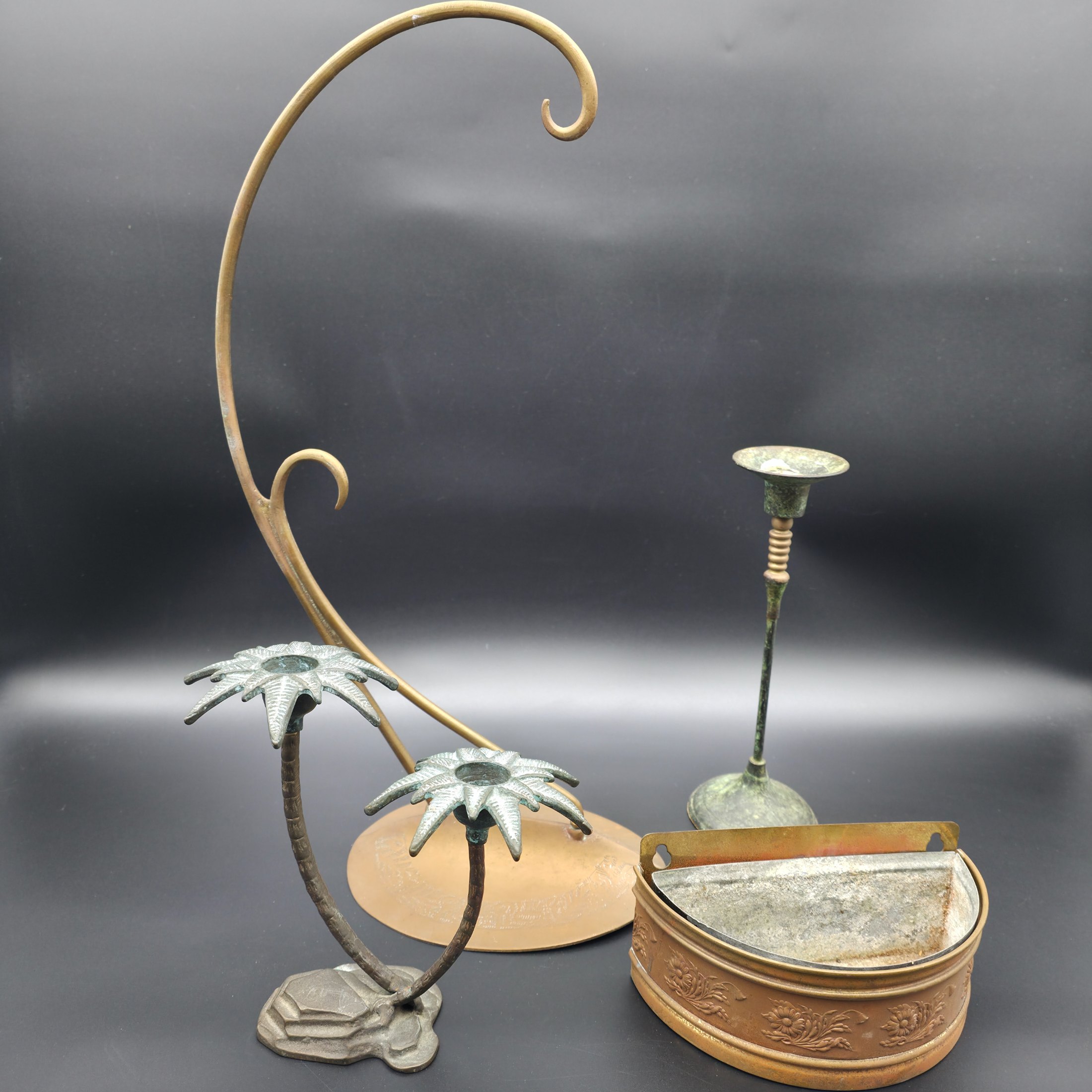 A varied collection of vintage metal decorative items including two palm tree-shaped candle holders, a tall candlestick, a curved display stand, and a wall-mounted brass matchbox.