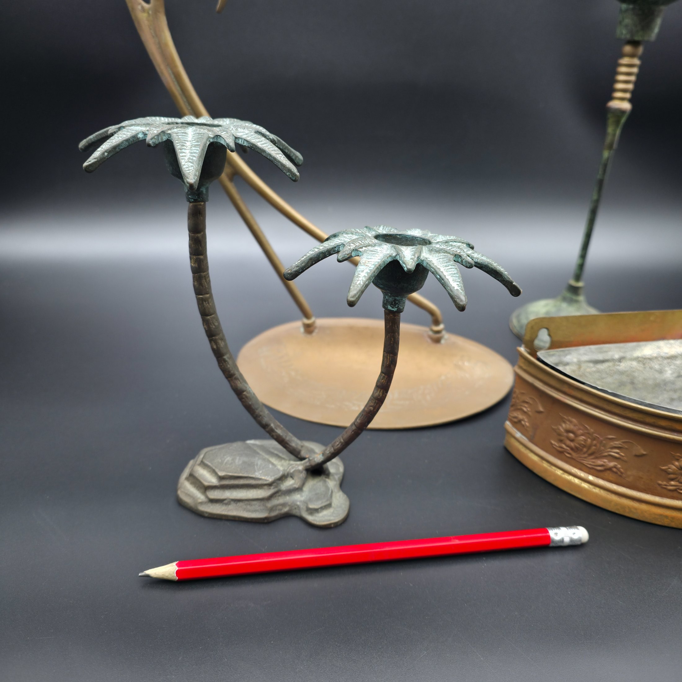 A varied collection of vintage metal decorative items including two palm tree-shaped candle holders, a tall candlestick, a curved display stand, and a wall-mounted brass matchbox. - View 2