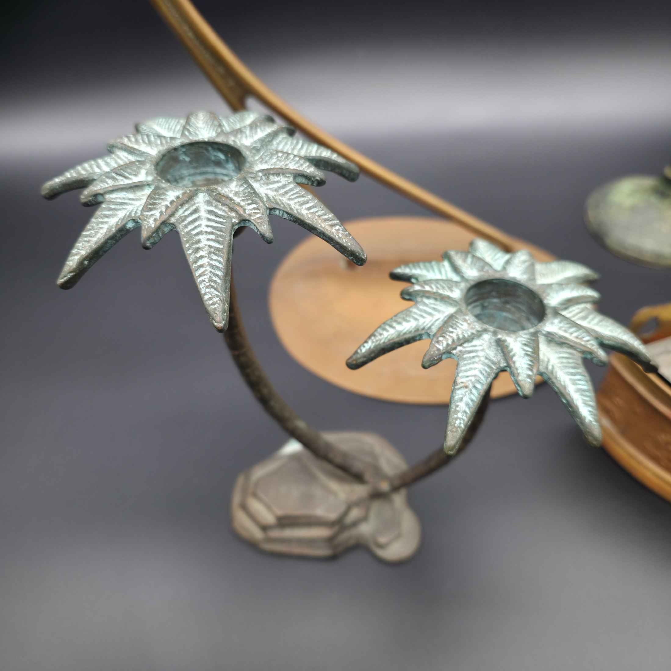 A varied collection of vintage metal decorative items including two palm tree-shaped candle holders, a tall candlestick, a curved display stand, and a wall-mounted brass matchbox. - View 3