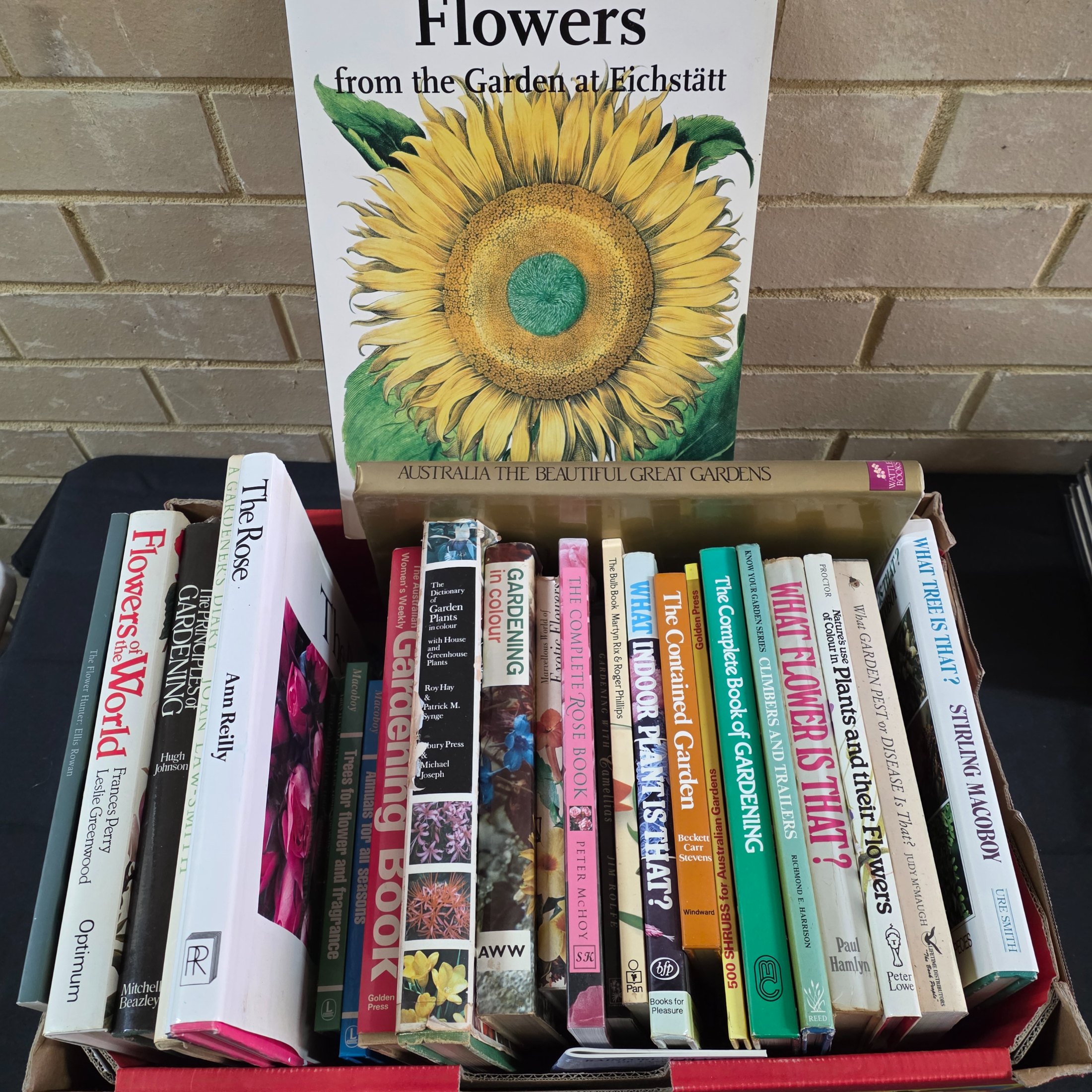 A box containing approximately 20-25 assorted gardening books, including titles on flowers, plant identification, and general horticultural practices.