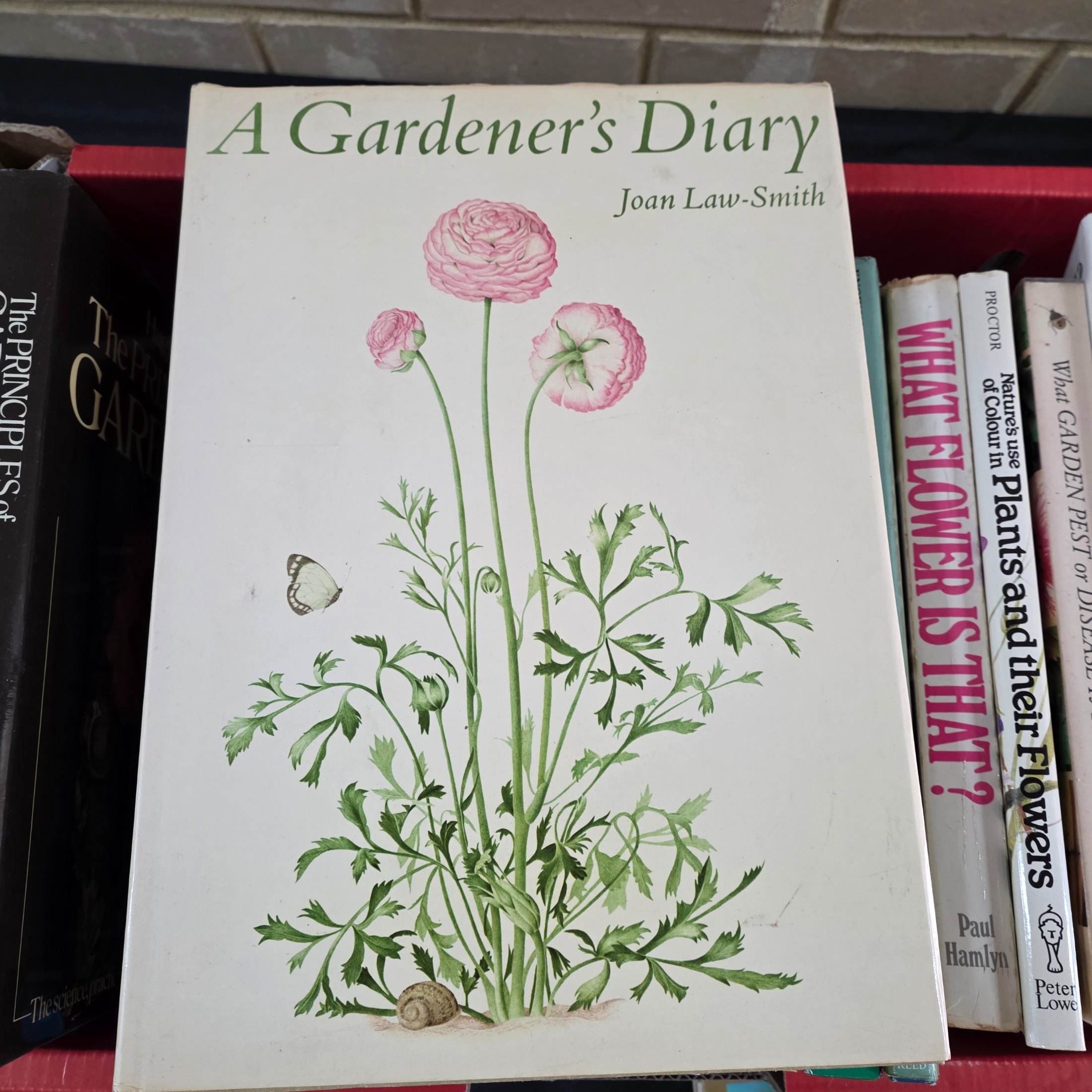 A box containing approximately 20-25 assorted gardening books, including titles on flowers, plant identification, and general horticultural practices. - View 2