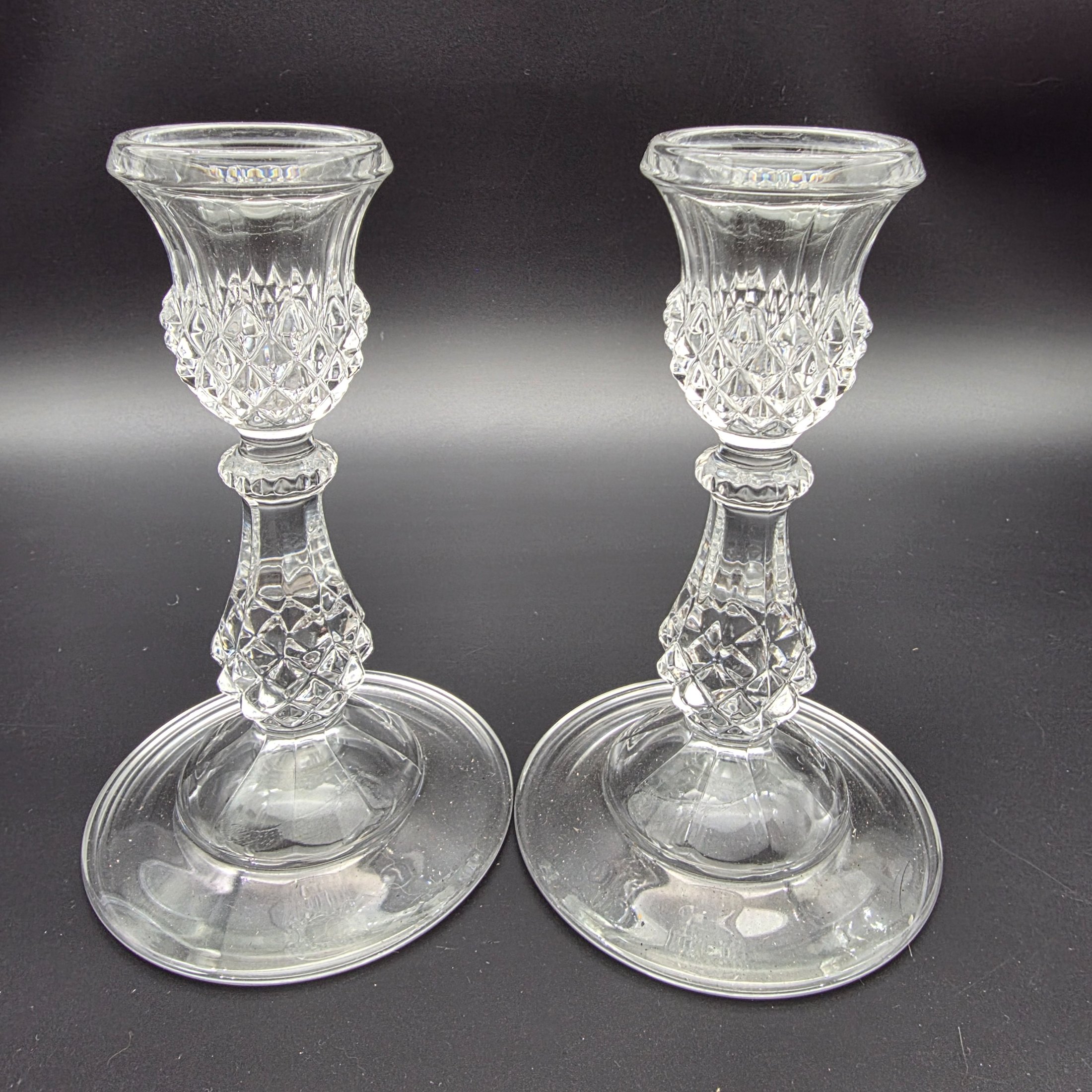 A diverse collection of clear and frosted pressed glass decorative items, comprising a pair of candlesticks, a small pitcher with metal handle and lid, a textured jar with a metal rim, and a rectangular vase with a frosted floral motif, likely from the early to mid-20th century. - View 2