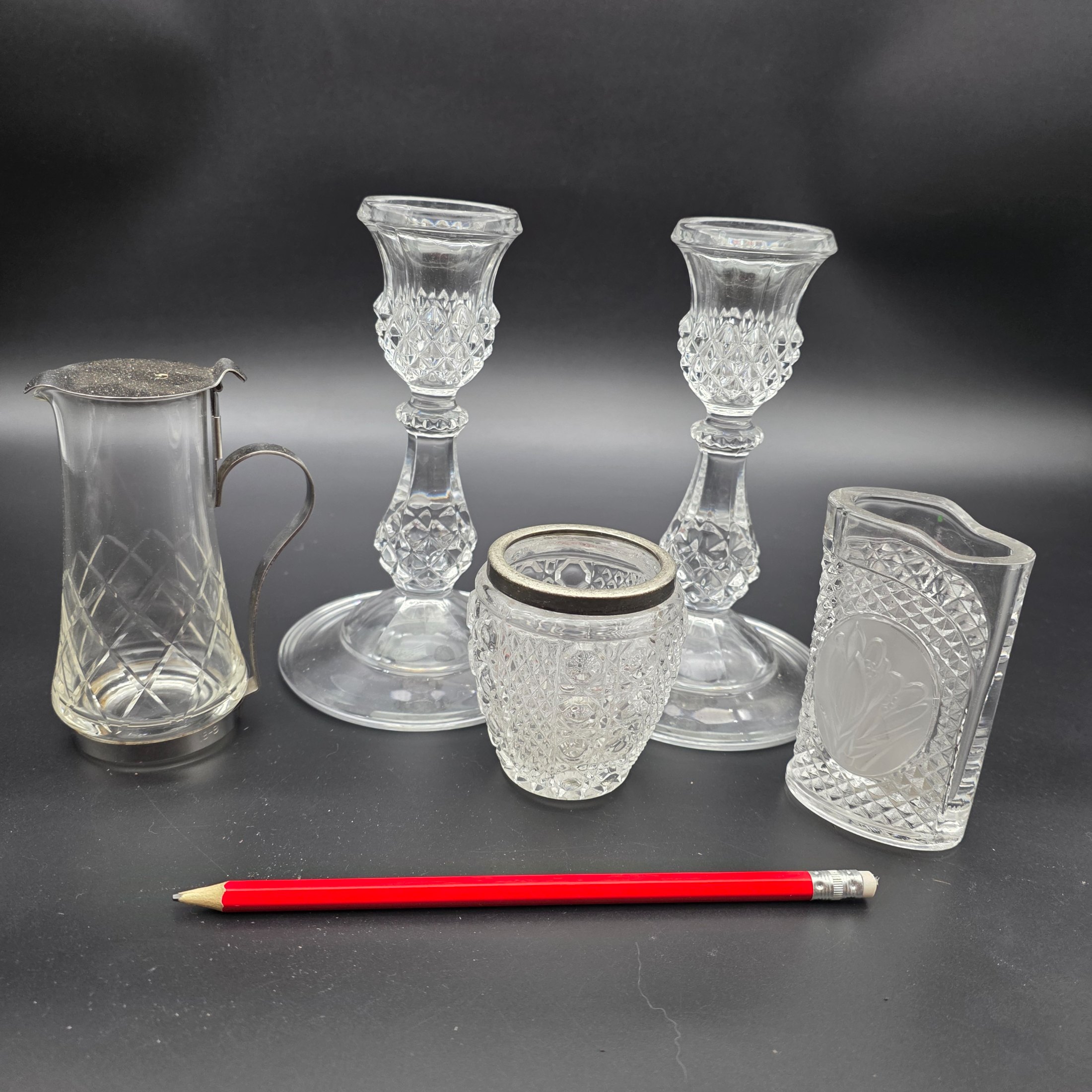 A diverse collection of clear and frosted pressed glass decorative items, comprising a pair of candlesticks, a small pitcher with metal handle and lid, a textured jar with a metal rim, and a rectangular vase with a frosted floral motif, likely from the early to mid-20th century. - View 4