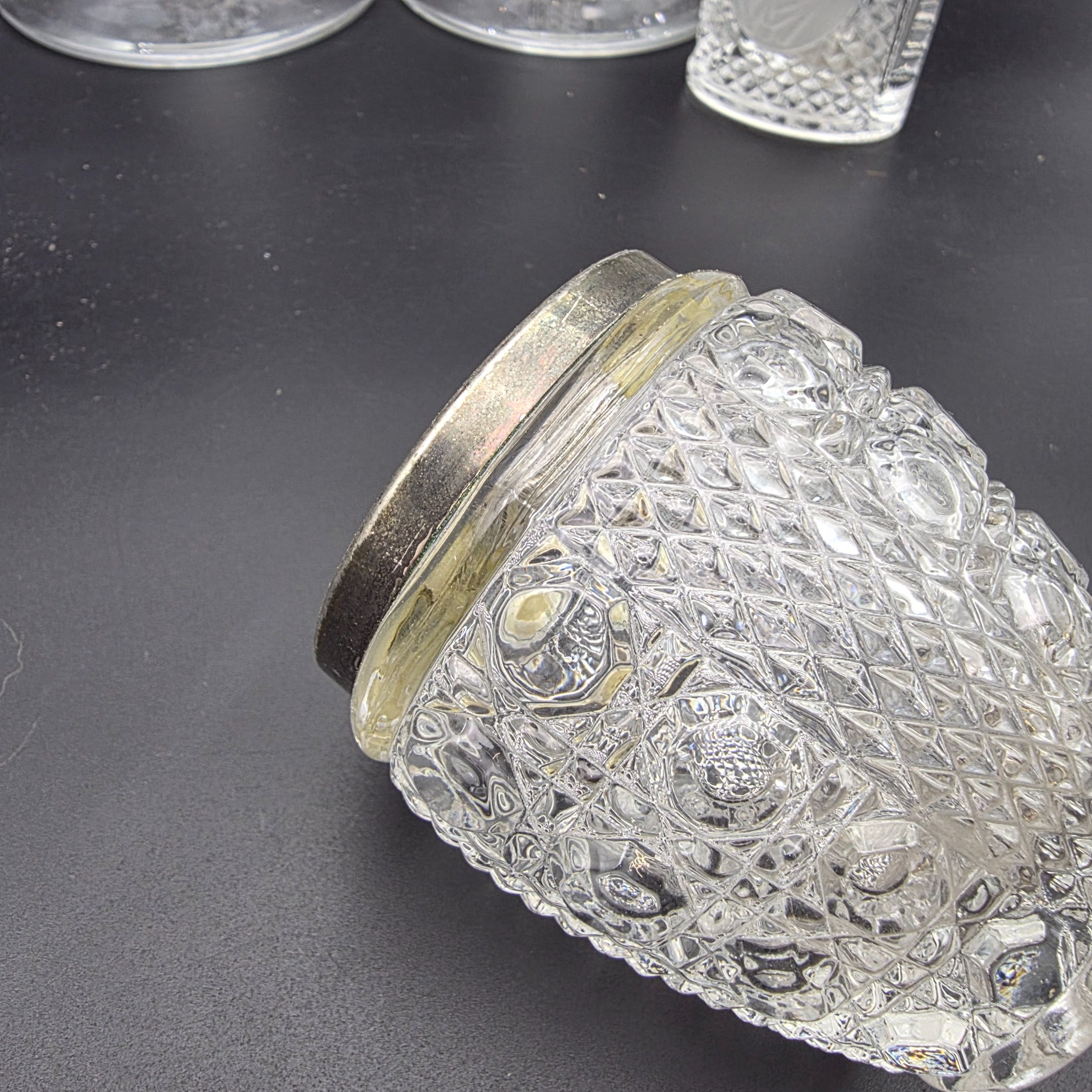 A diverse collection of clear and frosted pressed glass decorative items, comprising a pair of candlesticks, a small pitcher with metal handle and lid, a textured jar with a metal rim, and a rectangular vase with a frosted floral motif, likely from the early to mid-20th century. - View 8