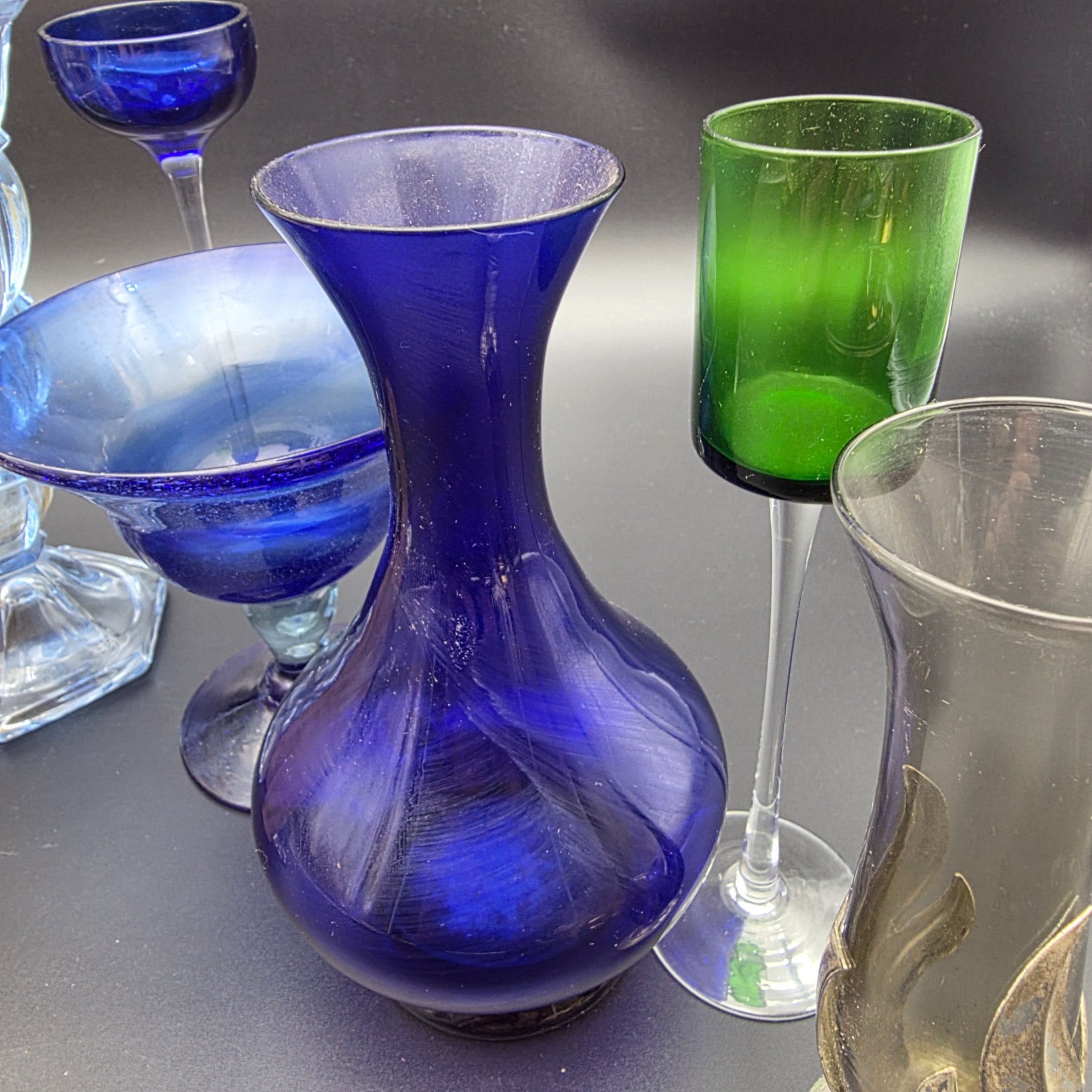 A varied collection of ten vintage coloured glass pieces, including vases, bowls, and stemmed glasses, showcasing different styles and manufacturing techniques from the mid-20th century. The array features shades of cobalt blue, amber, yellow, green, and smoky grey, offering a diverse decorative grouping. - View 3