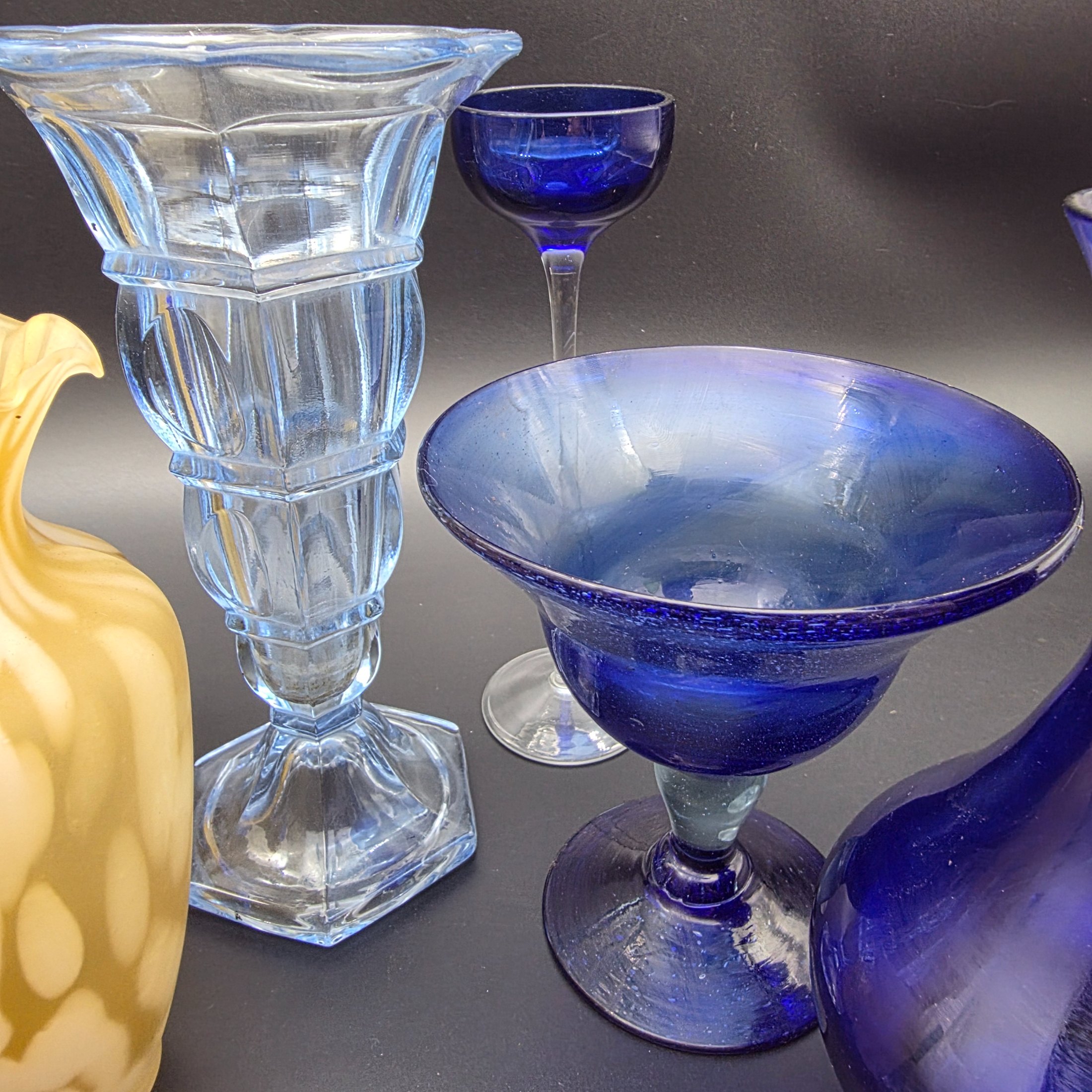 A varied collection of ten vintage coloured glass pieces, including vases, bowls, and stemmed glasses, showcasing different styles and manufacturing techniques from the mid-20th century. The array features shades of cobalt blue, amber, yellow, green, and smoky grey, offering a diverse decorative grouping. - View 4