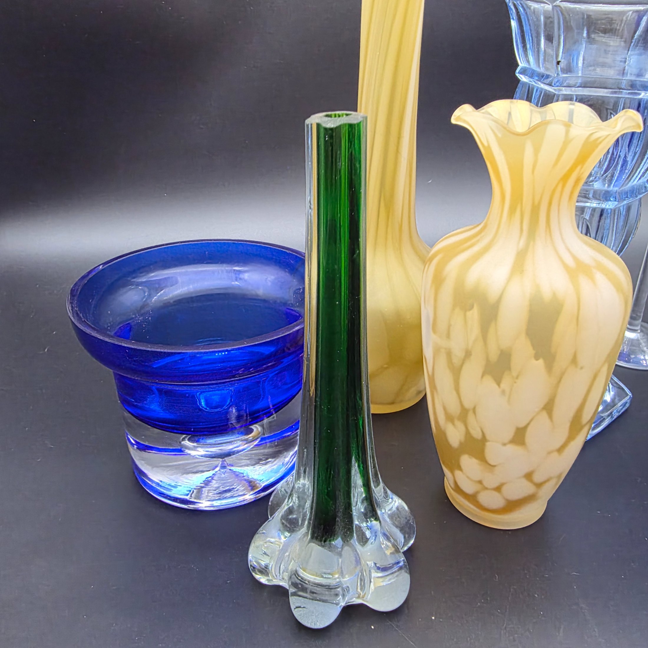 A varied collection of ten vintage coloured glass pieces, including vases, bowls, and stemmed glasses, showcasing different styles and manufacturing techniques from the mid-20th century. The array features shades of cobalt blue, amber, yellow, green, and smoky grey, offering a diverse decorative grouping. - View 5
