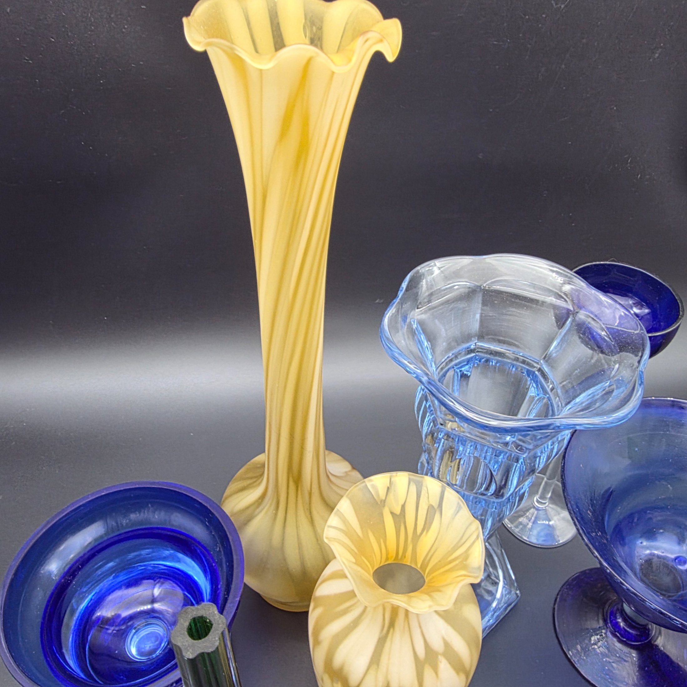 A varied collection of ten vintage coloured glass pieces, including vases, bowls, and stemmed glasses, showcasing different styles and manufacturing techniques from the mid-20th century. The array features shades of cobalt blue, amber, yellow, green, and smoky grey, offering a diverse decorative grouping. - View 6