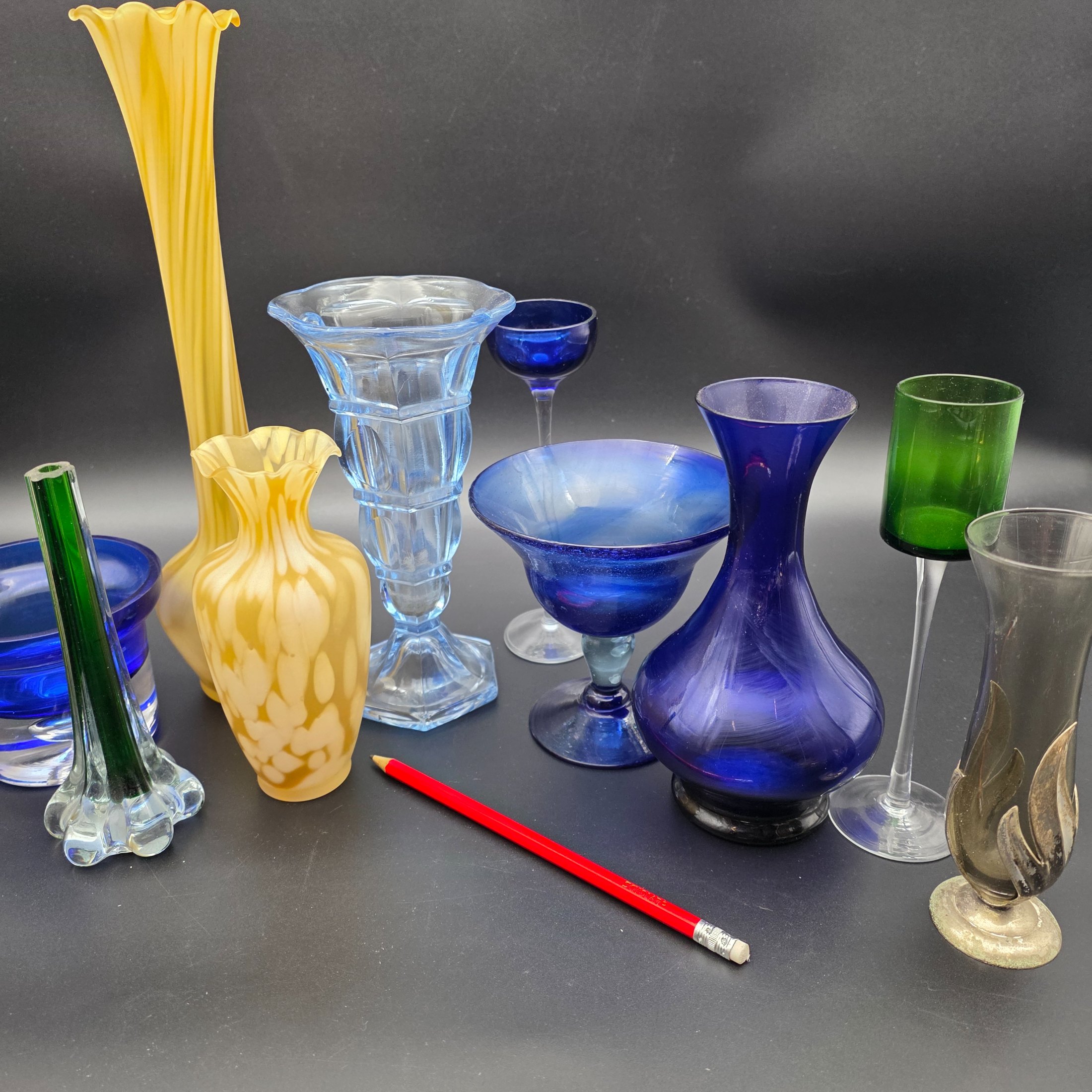 A varied collection of ten vintage coloured glass pieces, including vases, bowls, and stemmed glasses, showcasing different styles and manufacturing techniques from the mid-20th century. The array features shades of cobalt blue, amber, yellow, green, and smoky grey, offering a diverse decorative grouping. - View 7