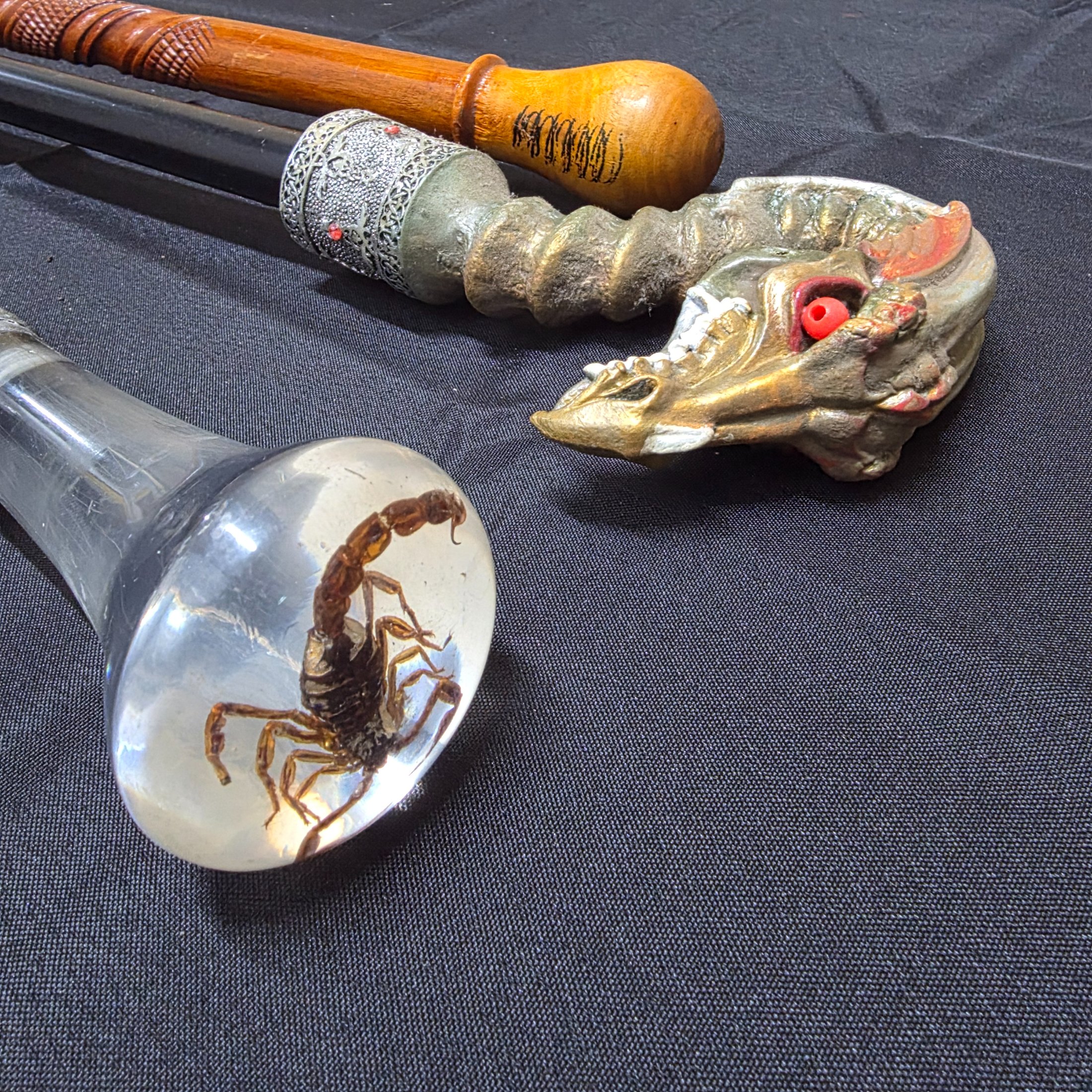 A collection of three vintage decorative walking sticks, featuring a carved wooden handle, a dragon-head handle, and a clear resin handle with an embedded scorpion.