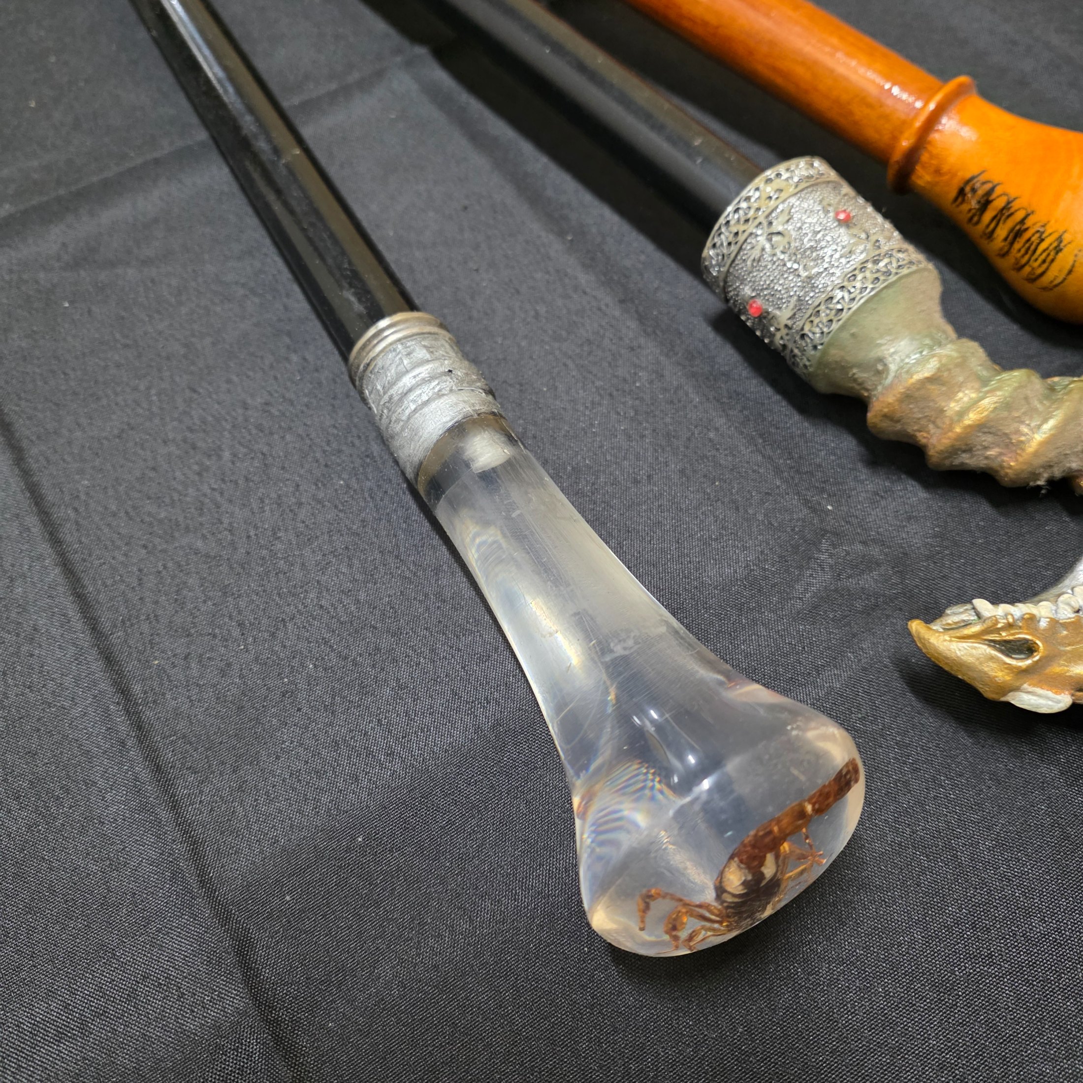 A collection of three vintage decorative walking sticks, featuring a carved wooden handle, a dragon-head handle, and a clear resin handle with an embedded scorpion. - View 3