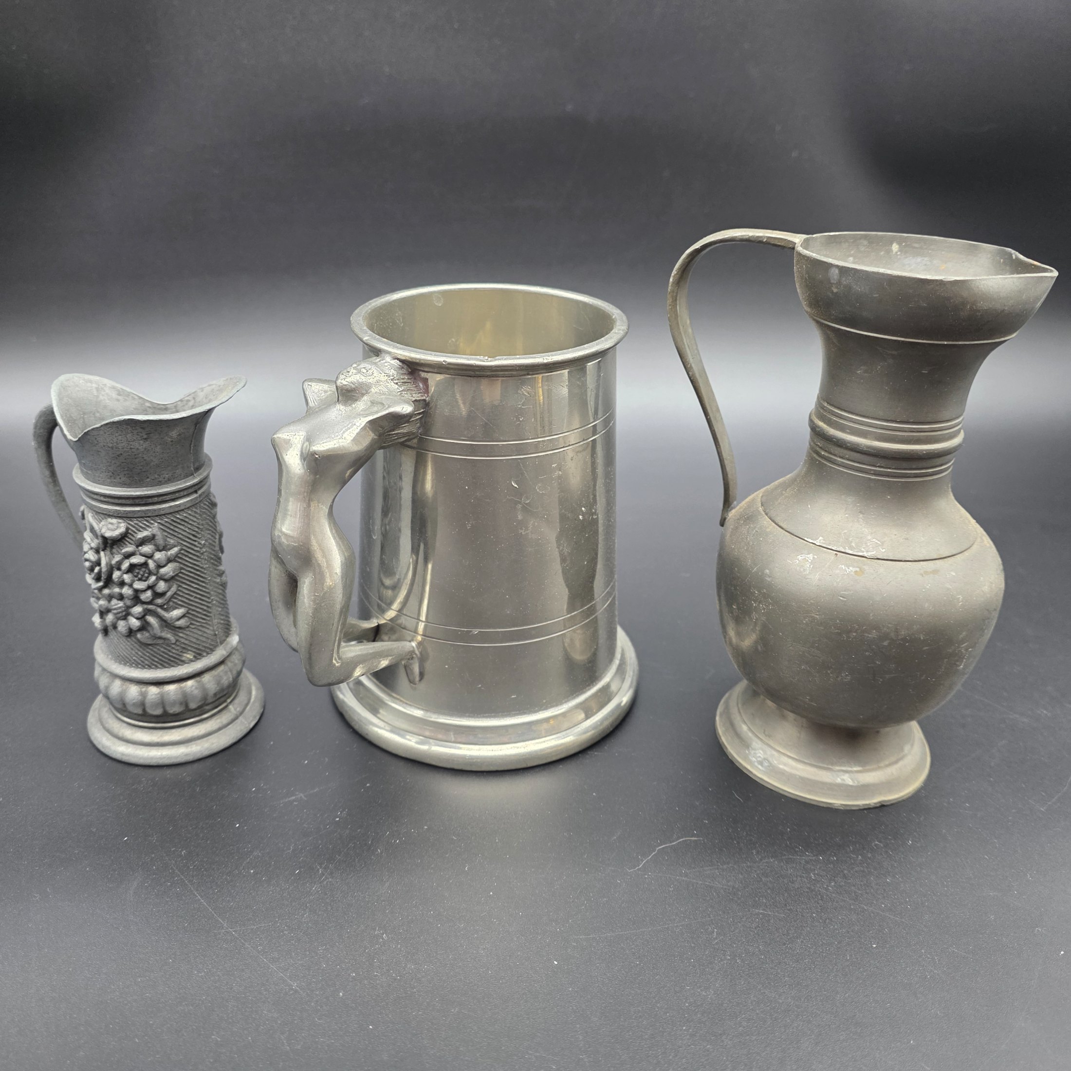 A collection of three traditional English pewter vessels, including a tankard with a unique nude figure handle, and two pitchers. These pieces originate from Sheffield, a city historically renowned for its metalwork and pewter manufacturing. - View 2
