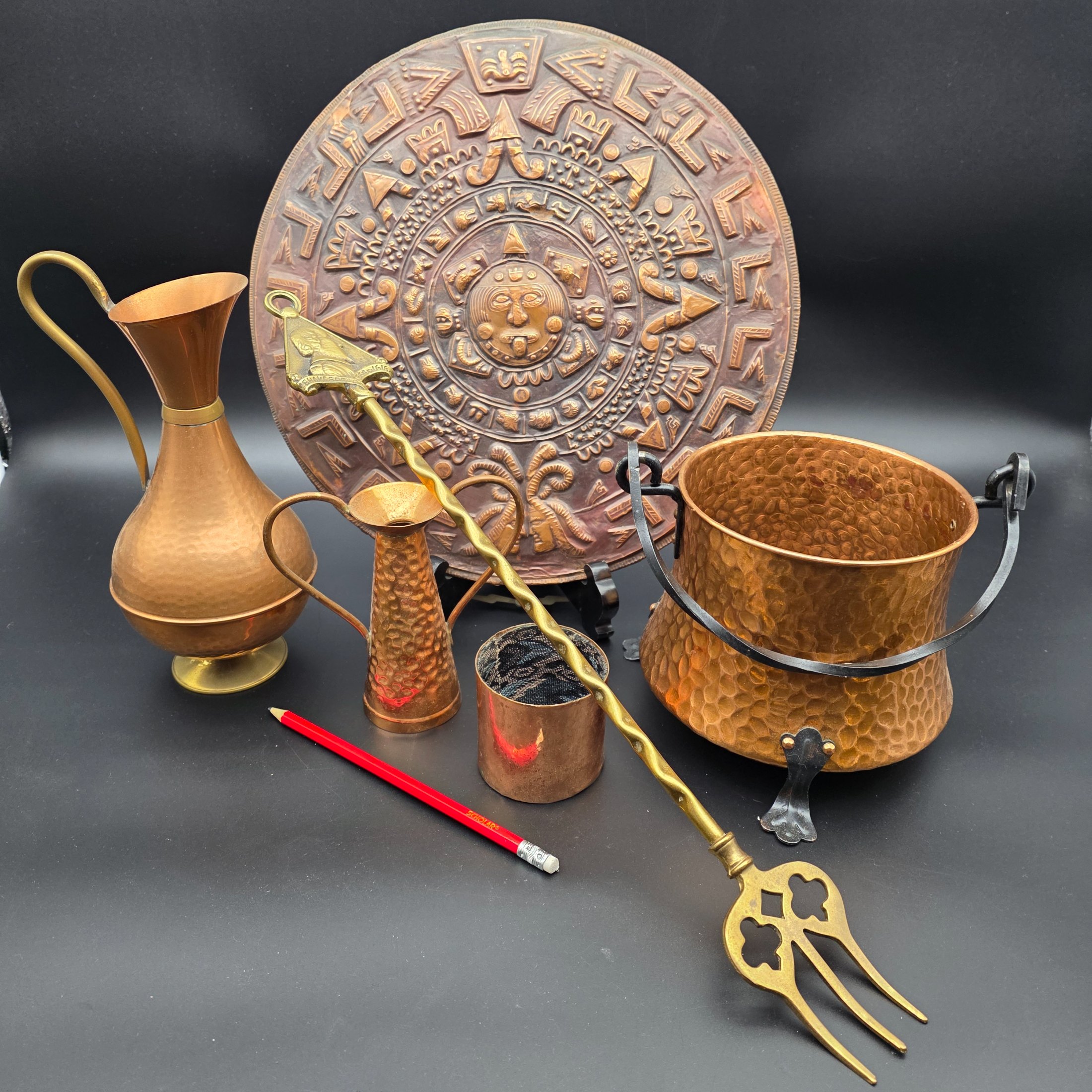 A collection of vintage copper and brass homewares, including an Aztec calendar wall hanging, pitchers, pots, and a Shakespeare-themed toasting fork. - View 2