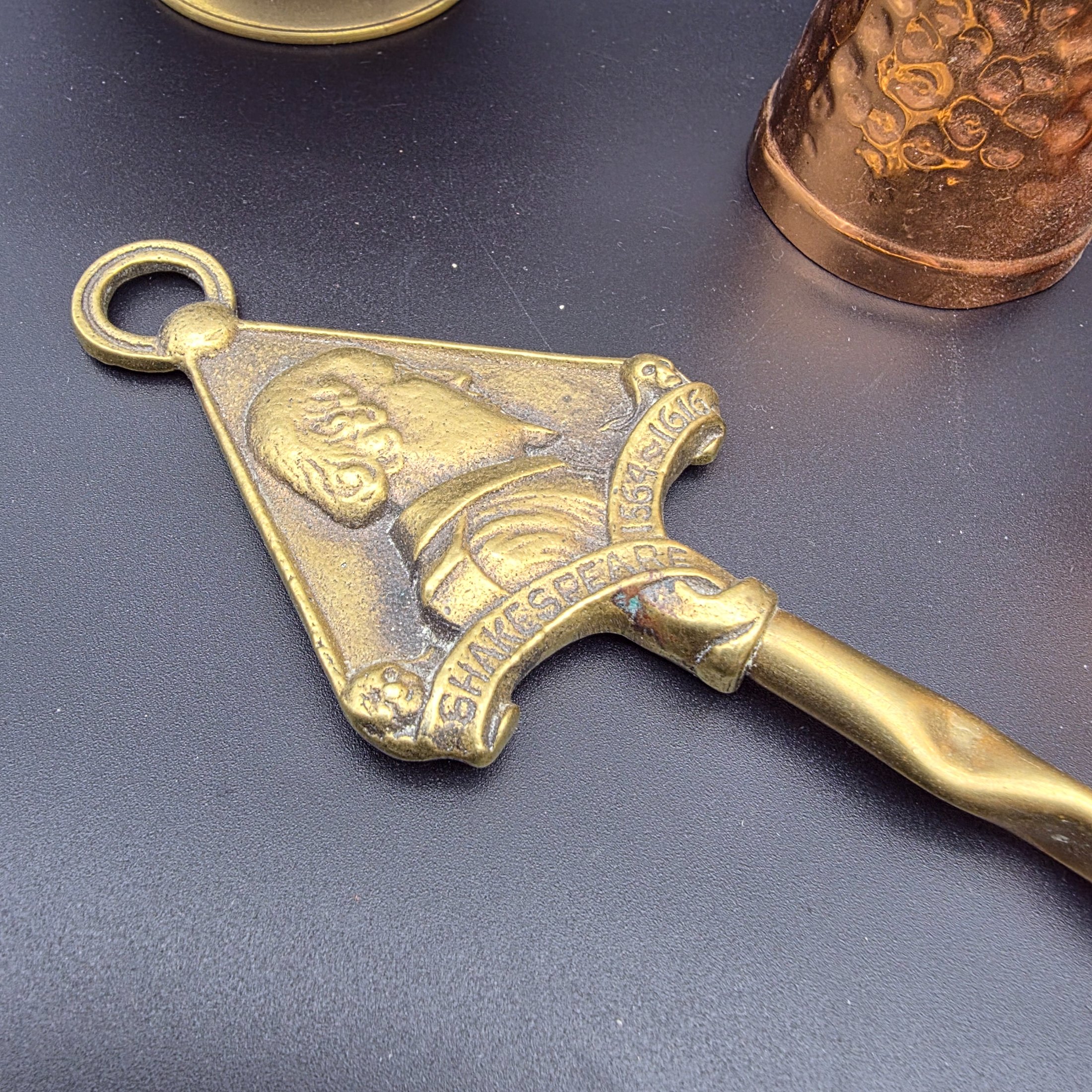 A collection of vintage copper and brass homewares, including an Aztec calendar wall hanging, pitchers, pots, and a Shakespeare-themed toasting fork. - View 3