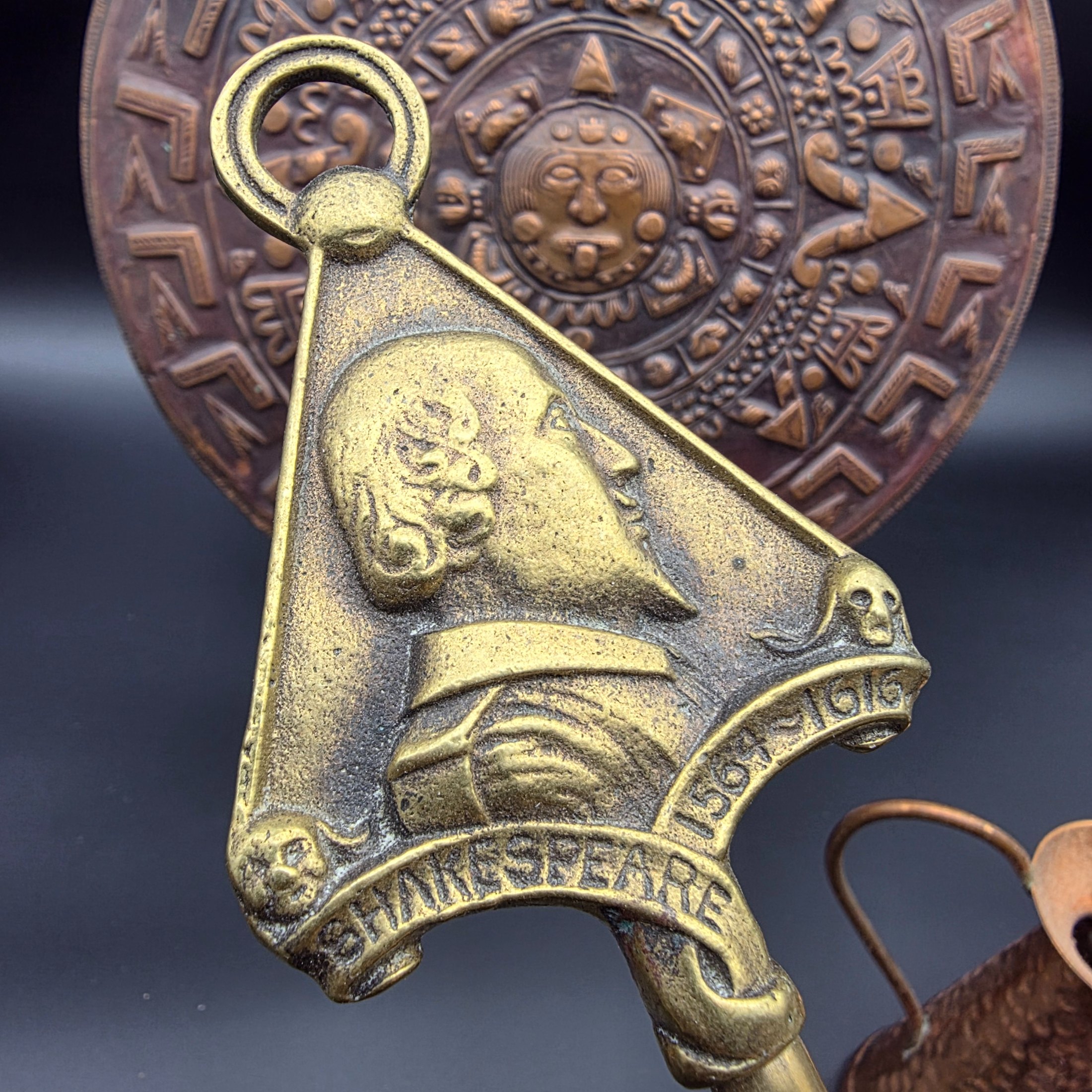 A collection of vintage copper and brass homewares, including an Aztec calendar wall hanging, pitchers, pots, and a Shakespeare-themed toasting fork. - View 4