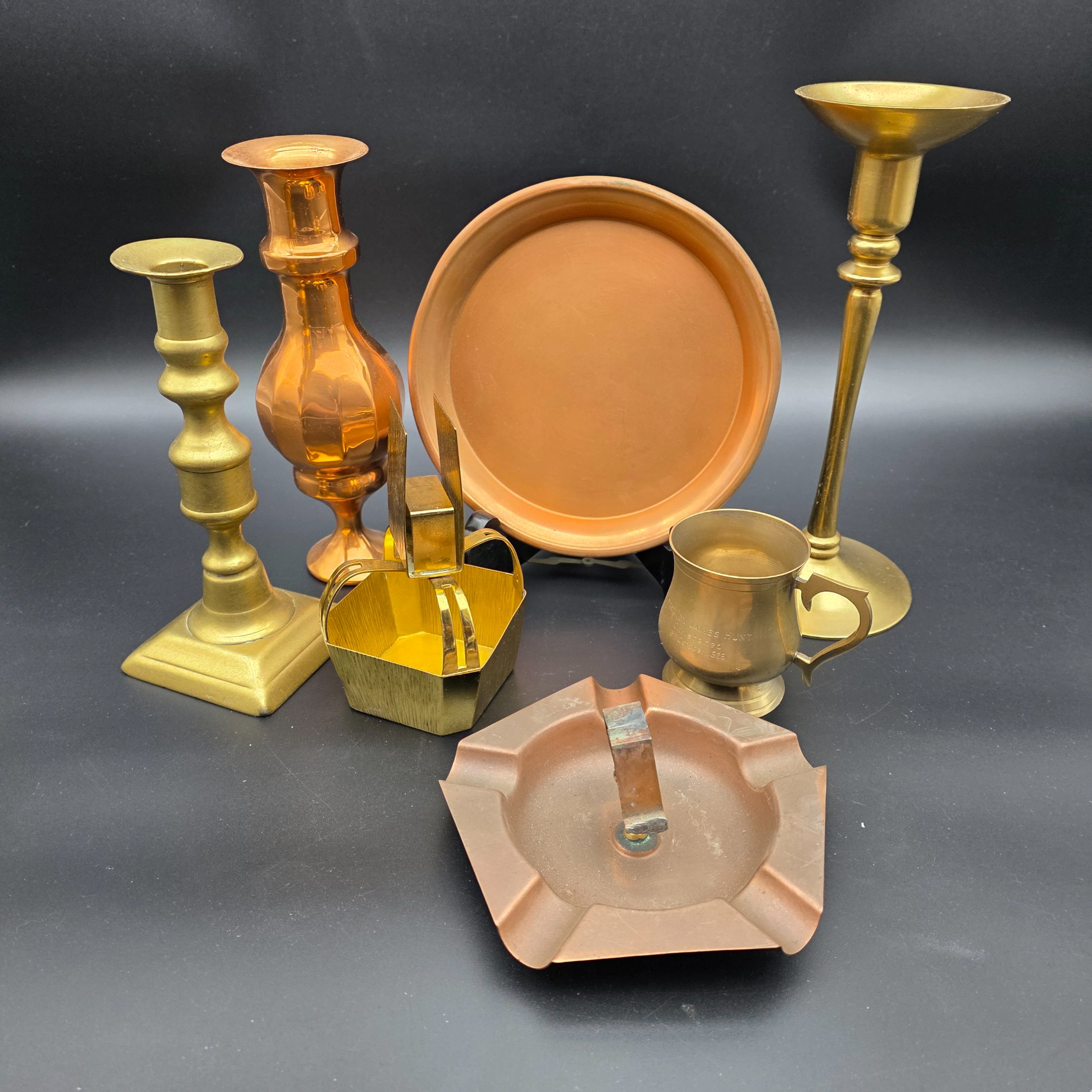 A collection of various vintage brass and copper sundries, including candlesticks, a decorative tray, a mug, an ashtray, and a small basket.
