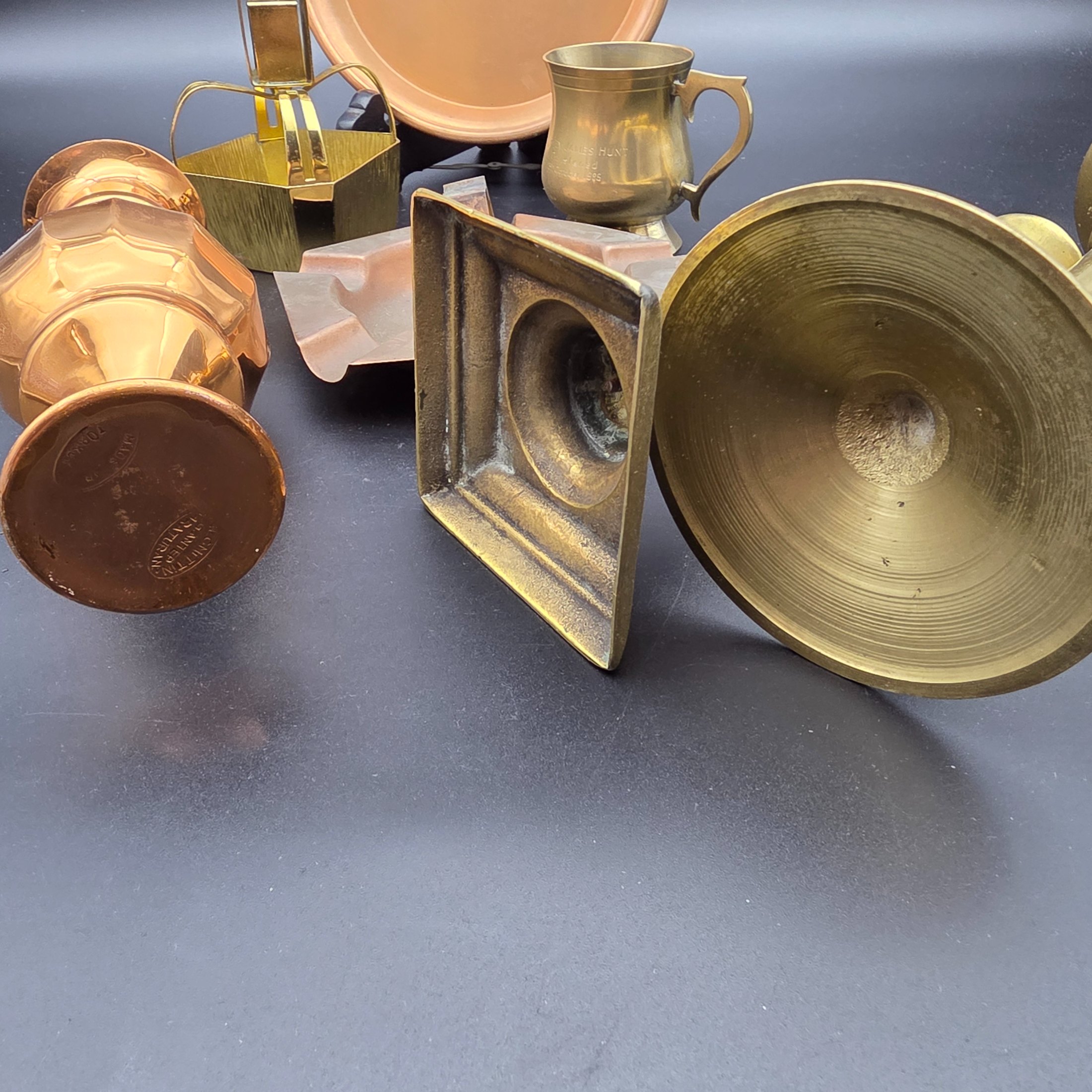 A collection of various vintage brass and copper sundries, including candlesticks, a decorative tray, a mug, an ashtray, and a small basket. - View 5