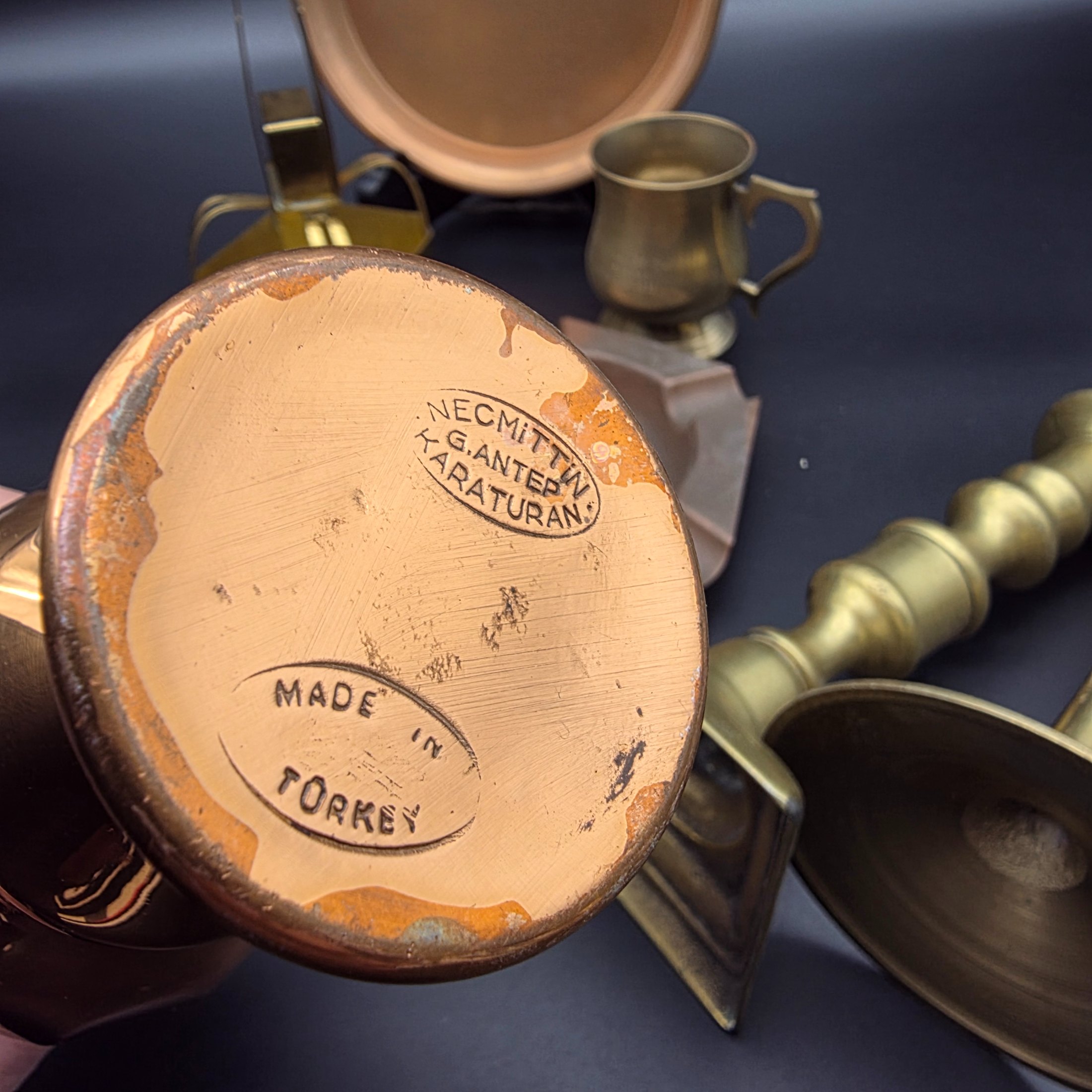 A collection of various vintage brass and copper sundries, including candlesticks, a decorative tray, a mug, an ashtray, and a small basket. - View 6