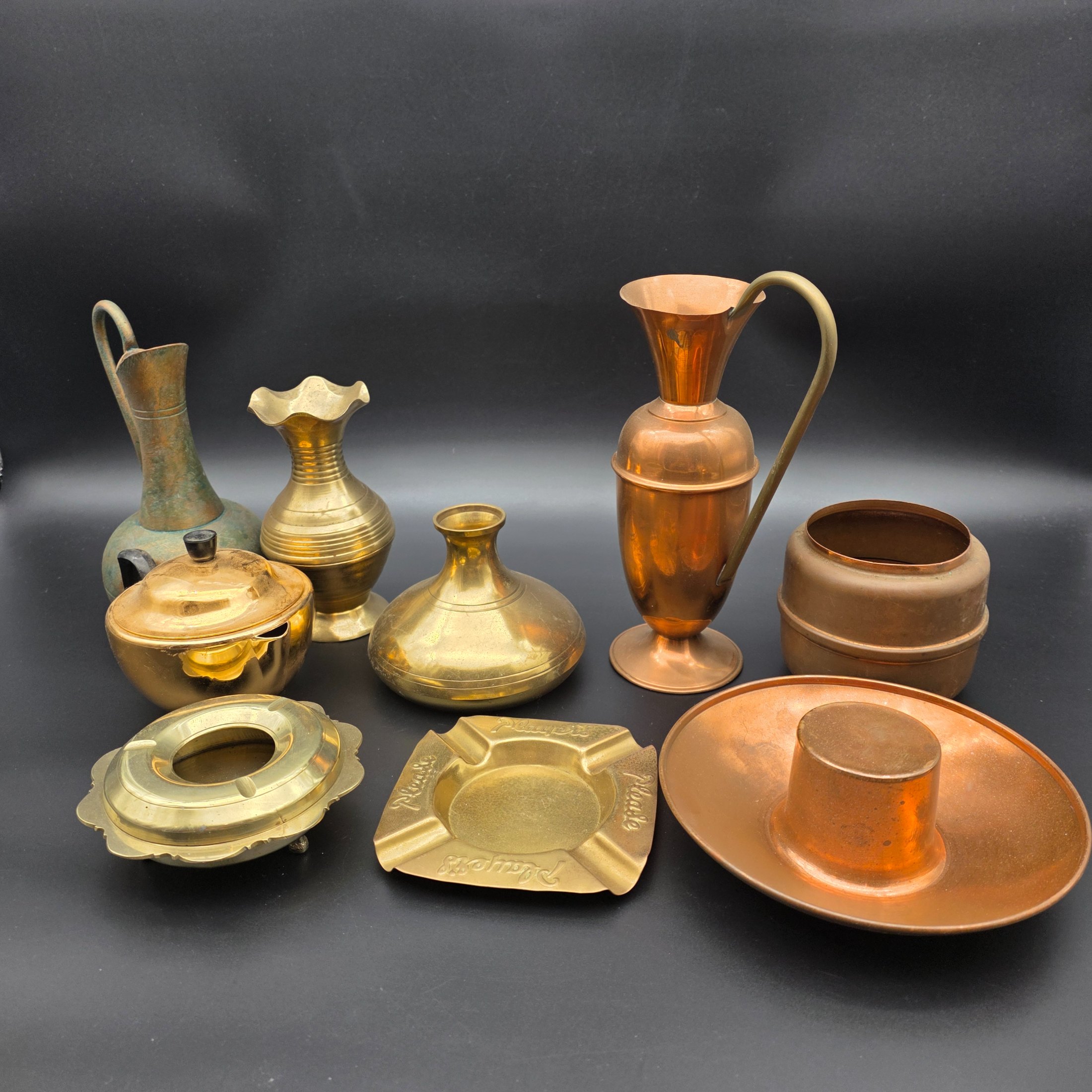 An appealing collection of eight assorted vintage brass and copper decorative items, including jugs, vases, pots, and ashtrays, showcasing varied forms and patinas from different eras and origins, ideal for display or use in period interiors. This lot includes an Australian-made Glama-Ware brass-finished stainless steel lidded pot and a 'Players' brand ashtray made in England.